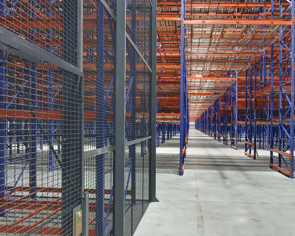 A pick tunnel through tall orange and blue metal shelving racks and a gated storage area.