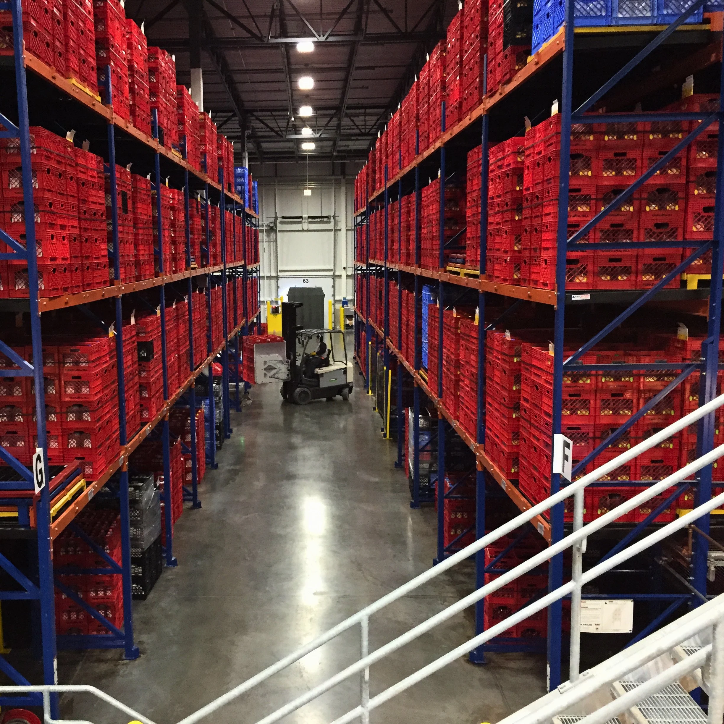 Forklift lifts pallets of beverage cartons from pushback rack.
