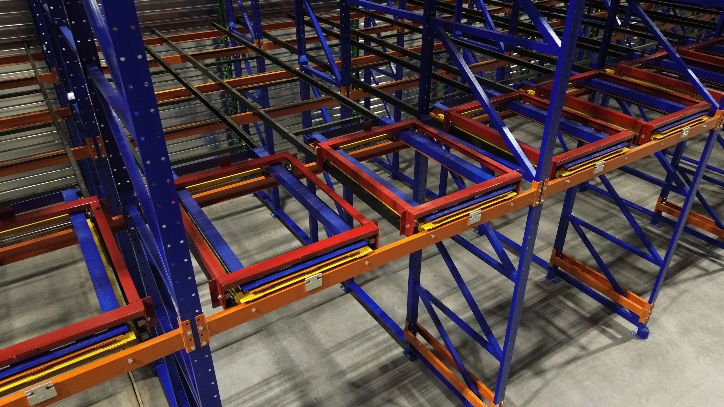 Pushback storage shelving with blue, orange, and yellow pushback frames and roller tracks, seen from above.