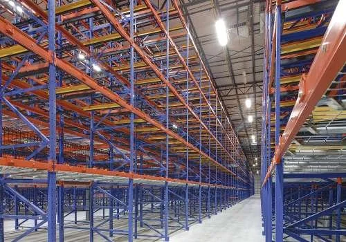 Empty industrial warehouse with tall, blue and orange pushback racking.