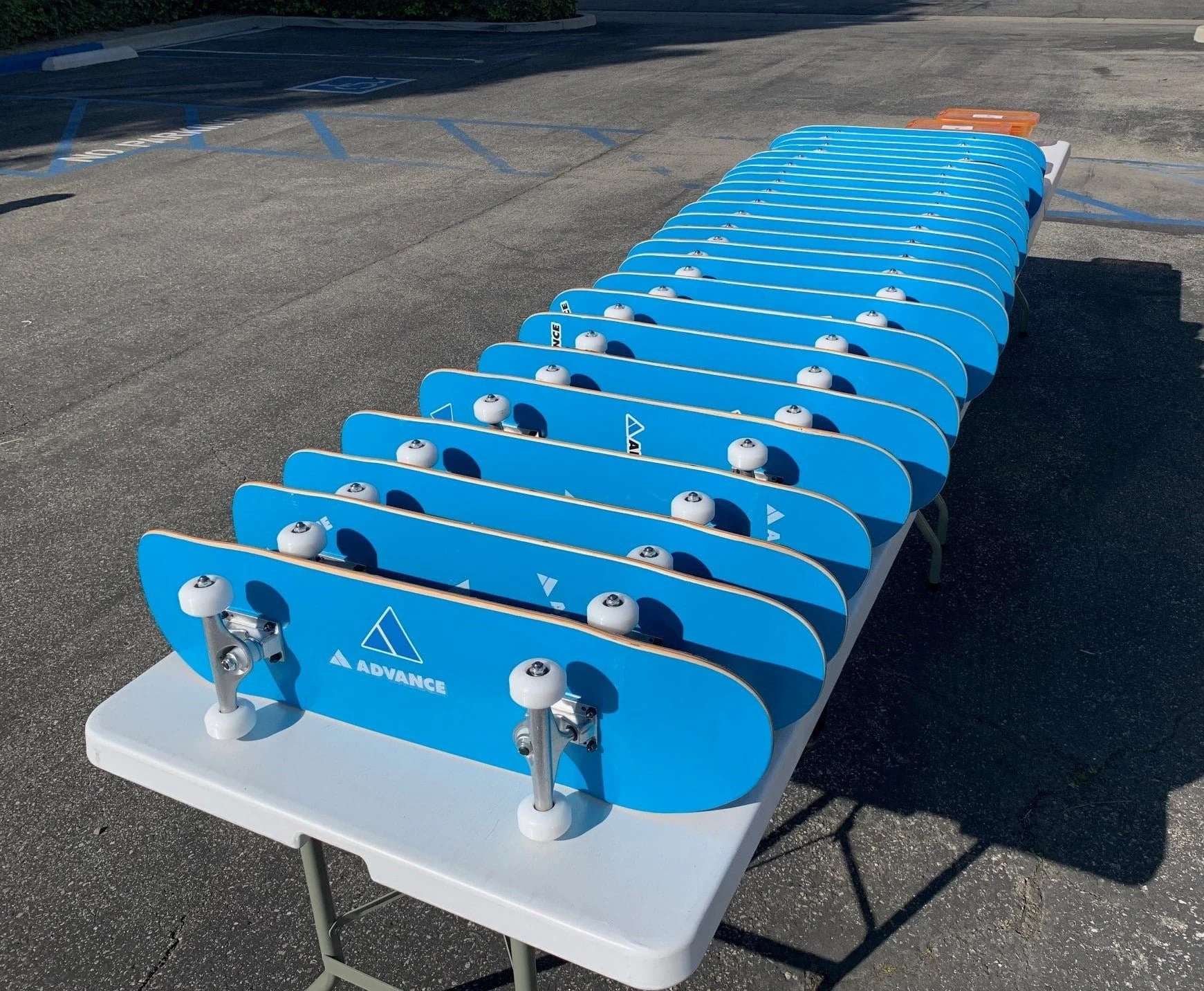 Row of blue skateboards with white wheels and the brand name 'Advance' on a display table in an outdoor parking lot.
