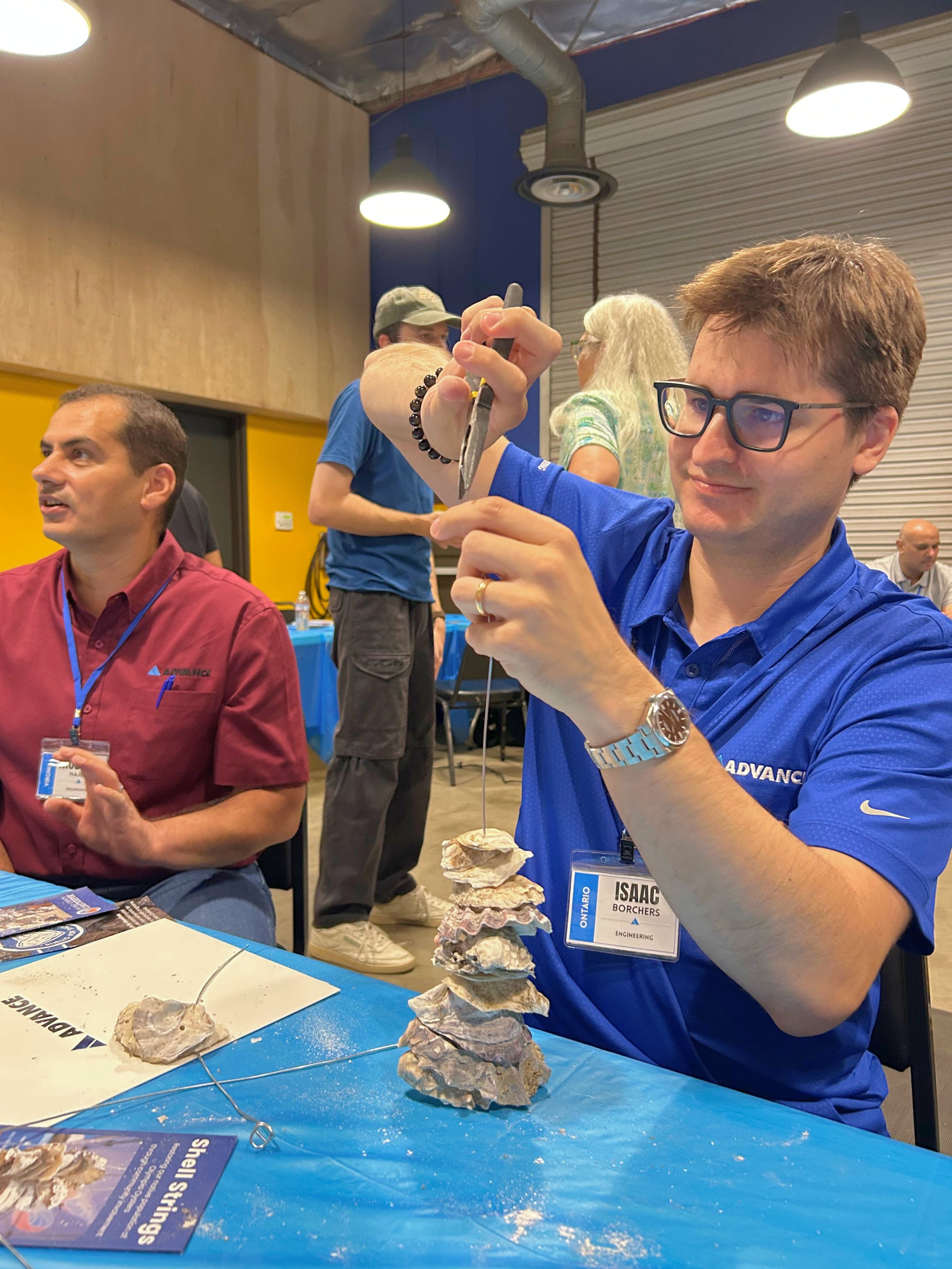 Employee puts together oysters on a metal wire with pliers.