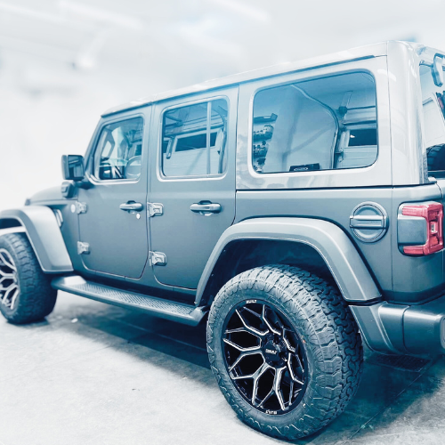 A black four-door Jeep SUV with large off-road tires and stylish black rims, parked indoors.