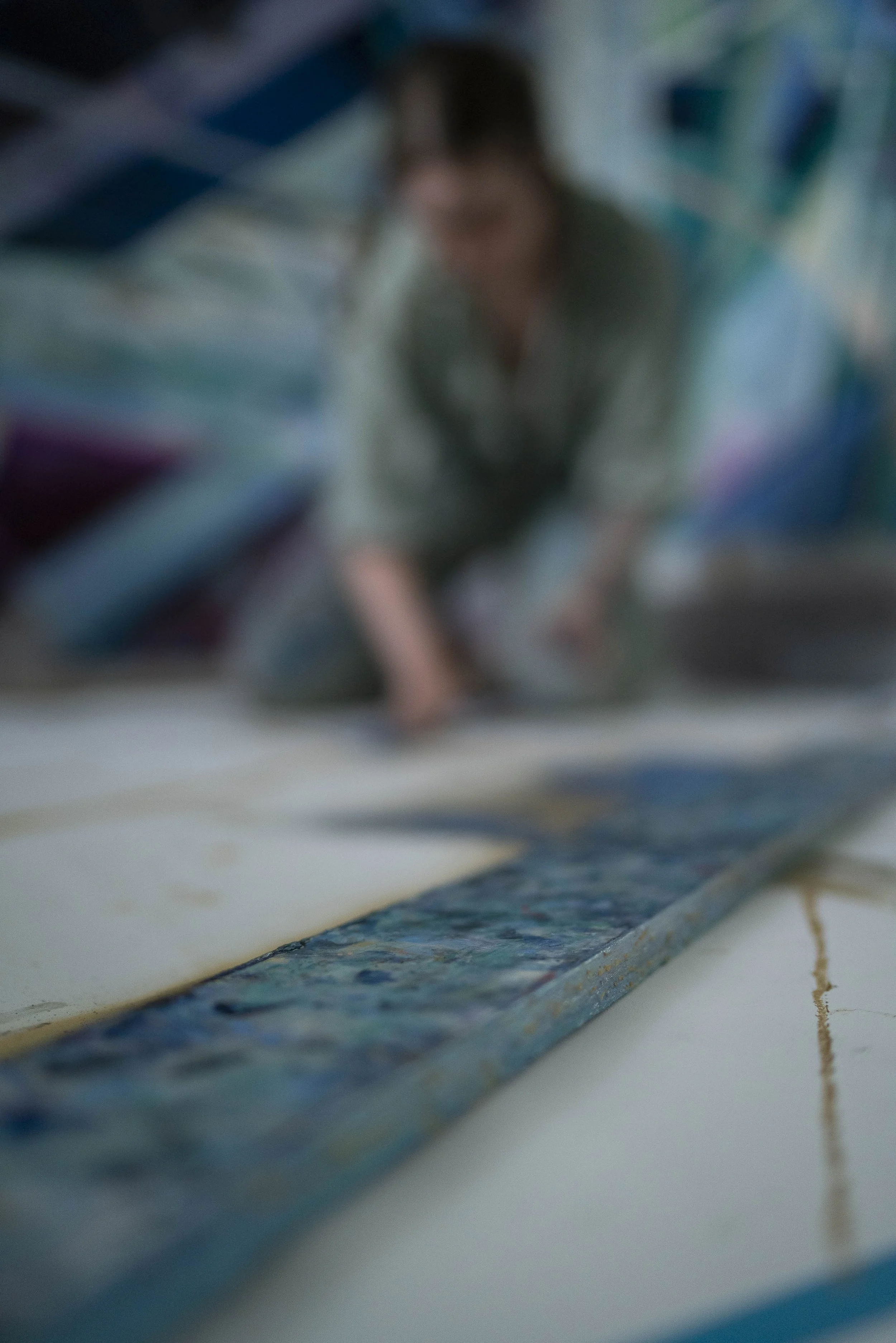 Nadia Ørneborg working on a large, colourful artwork on the floor, with paint and brushes visible.