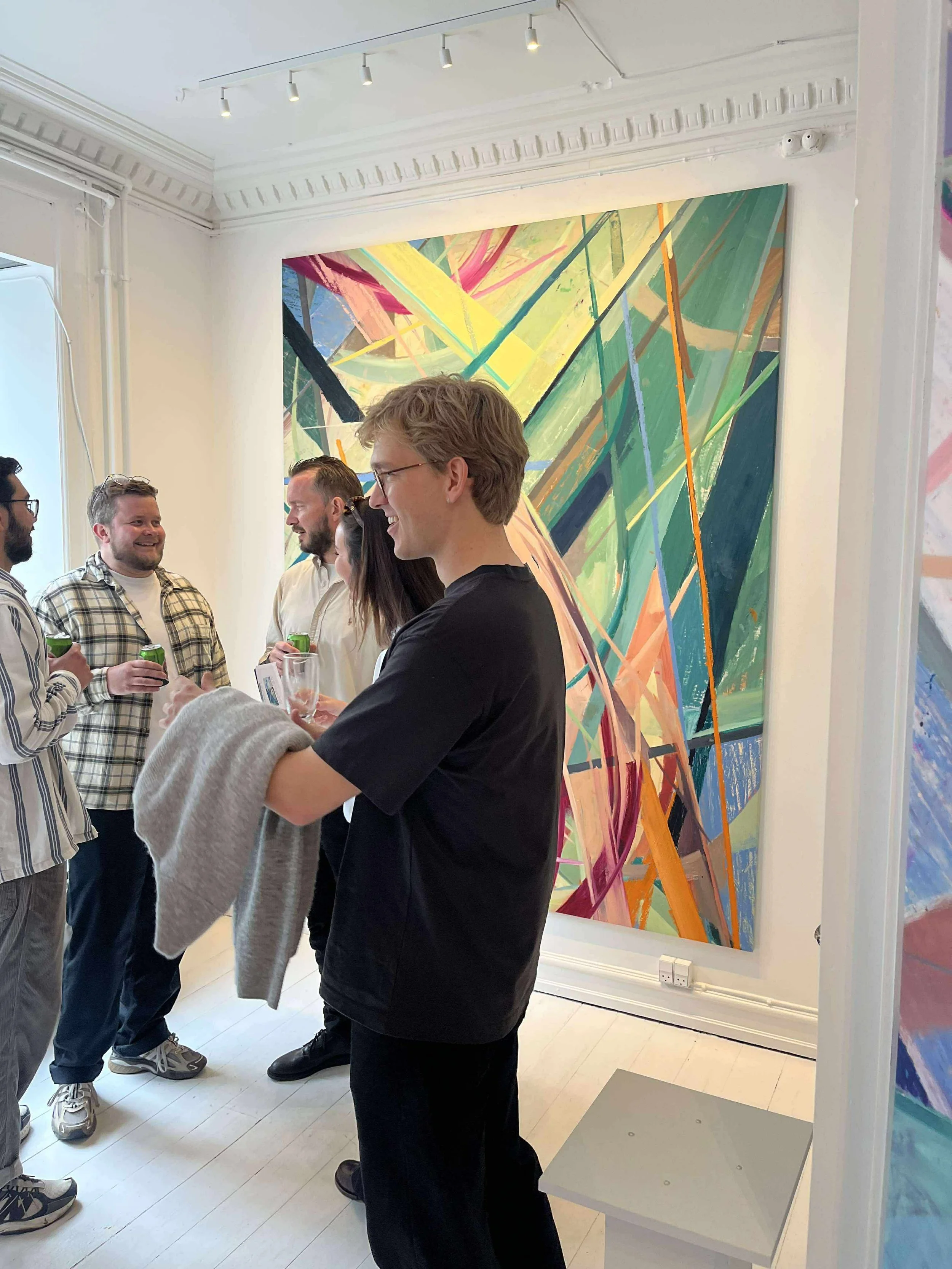 People socializing and chatting in an art gallery with a colorful abstract painting on the wall.