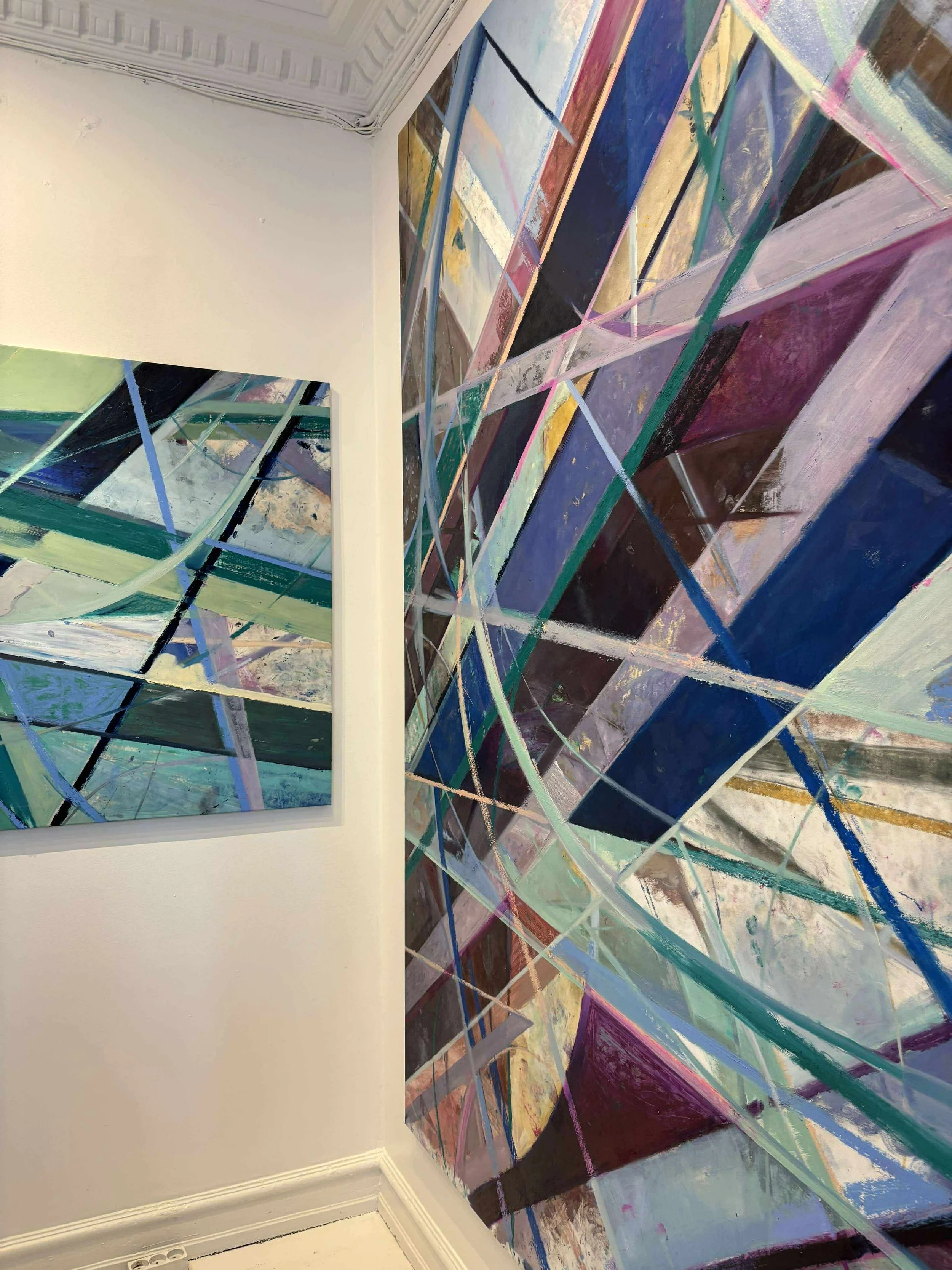 Close-up of an abstract geometric painting with overlapping colorful shapes and lines, mounted on a white gallery wall.