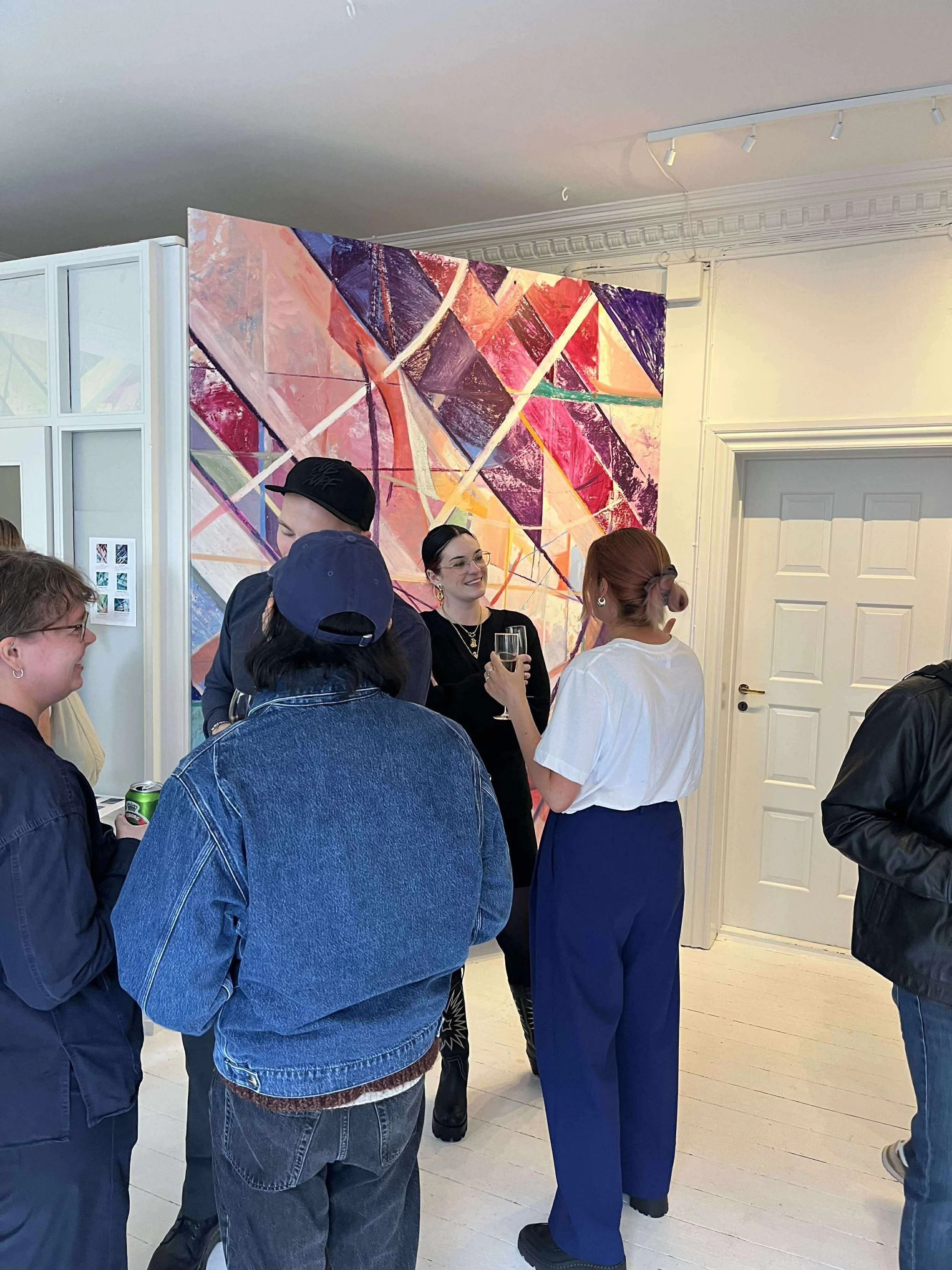 Group of people socializing at an art gallery with a colorful abstract painting in the background.