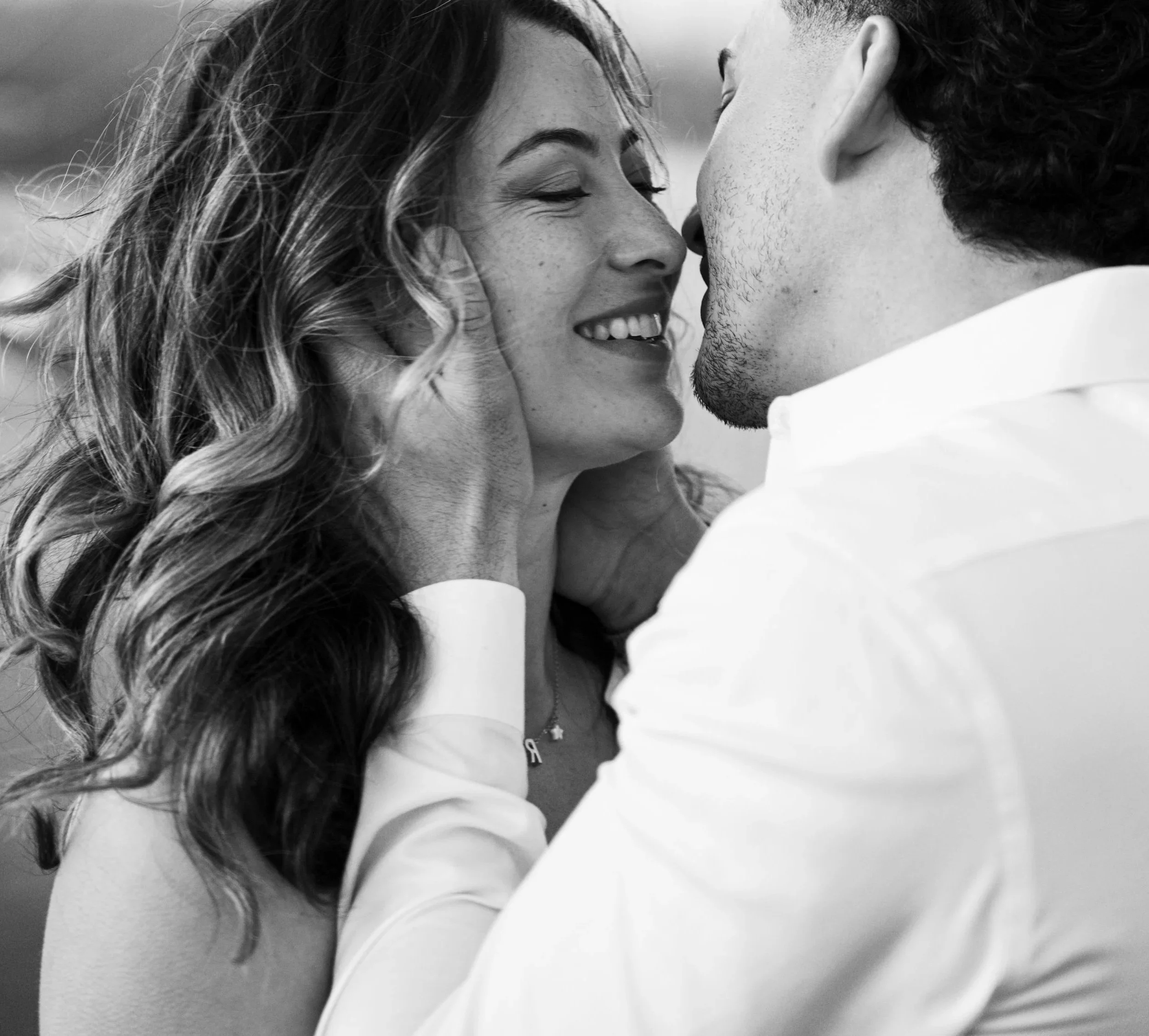 A black and white close-up photo of a couple about to kiss, with the woman smiling and holding the man's face gently.