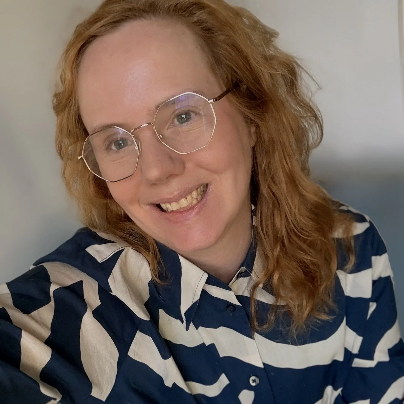 A woman with curly red hair, glasses, and a striped navy and white shirt smiling at the camera.