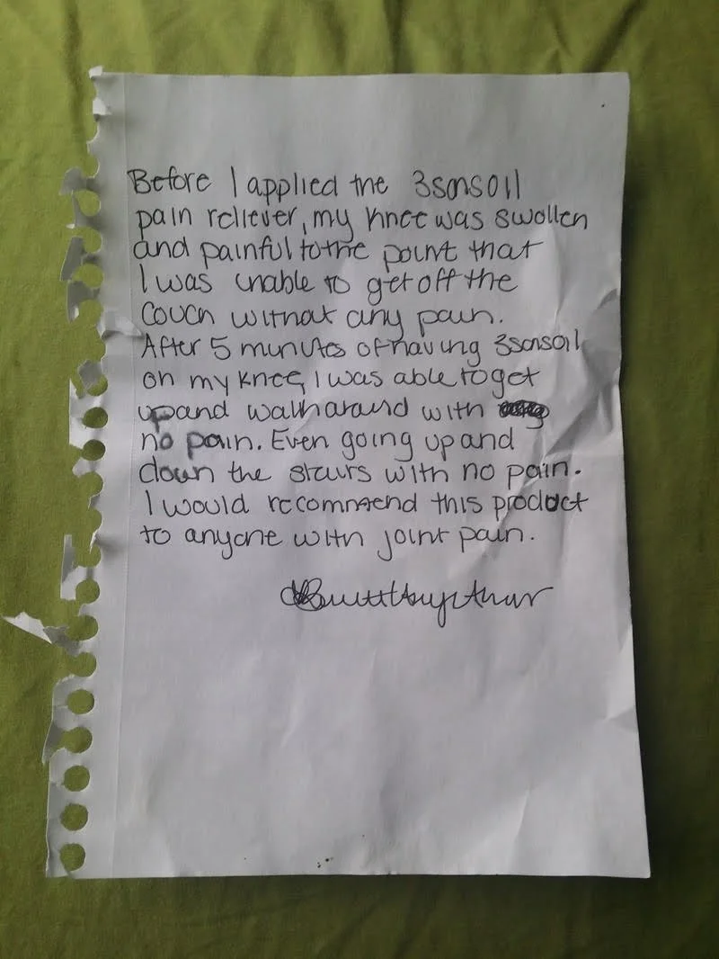 Handwritten note on a torn piece of notebook paper with perforations on the left, placed on a green fabric background. The note describes experience with a product and ends with a signature.