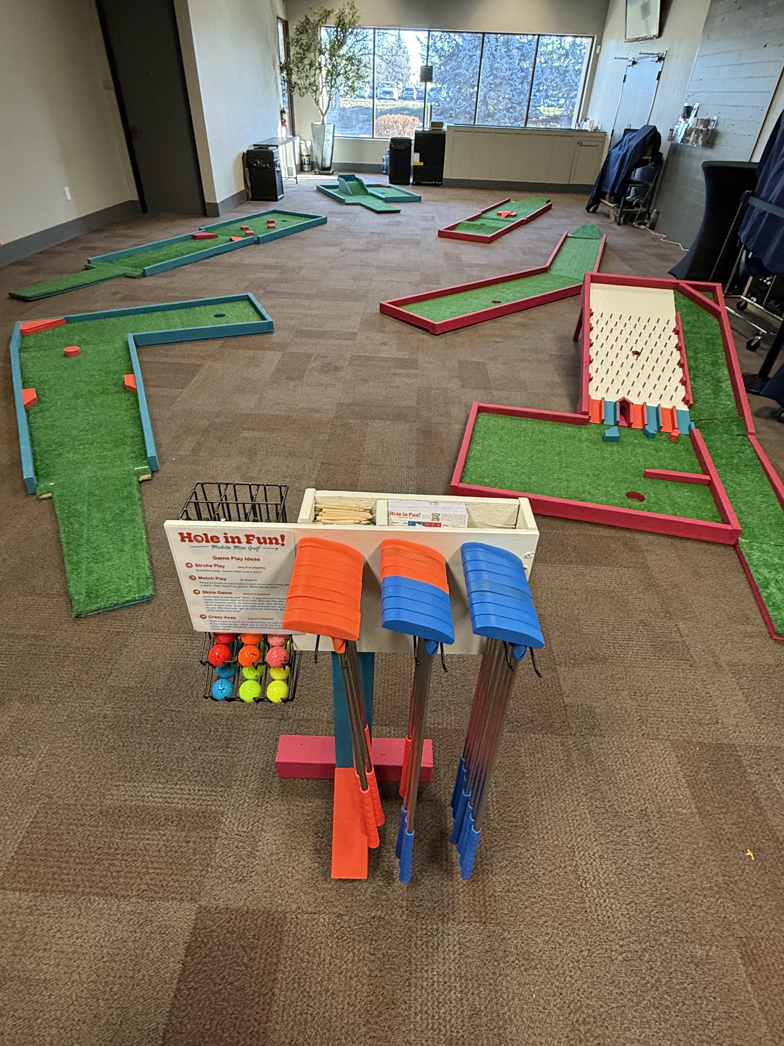 Indoor mini golf course with multiple holes and a rack of golf balls in the foreground.