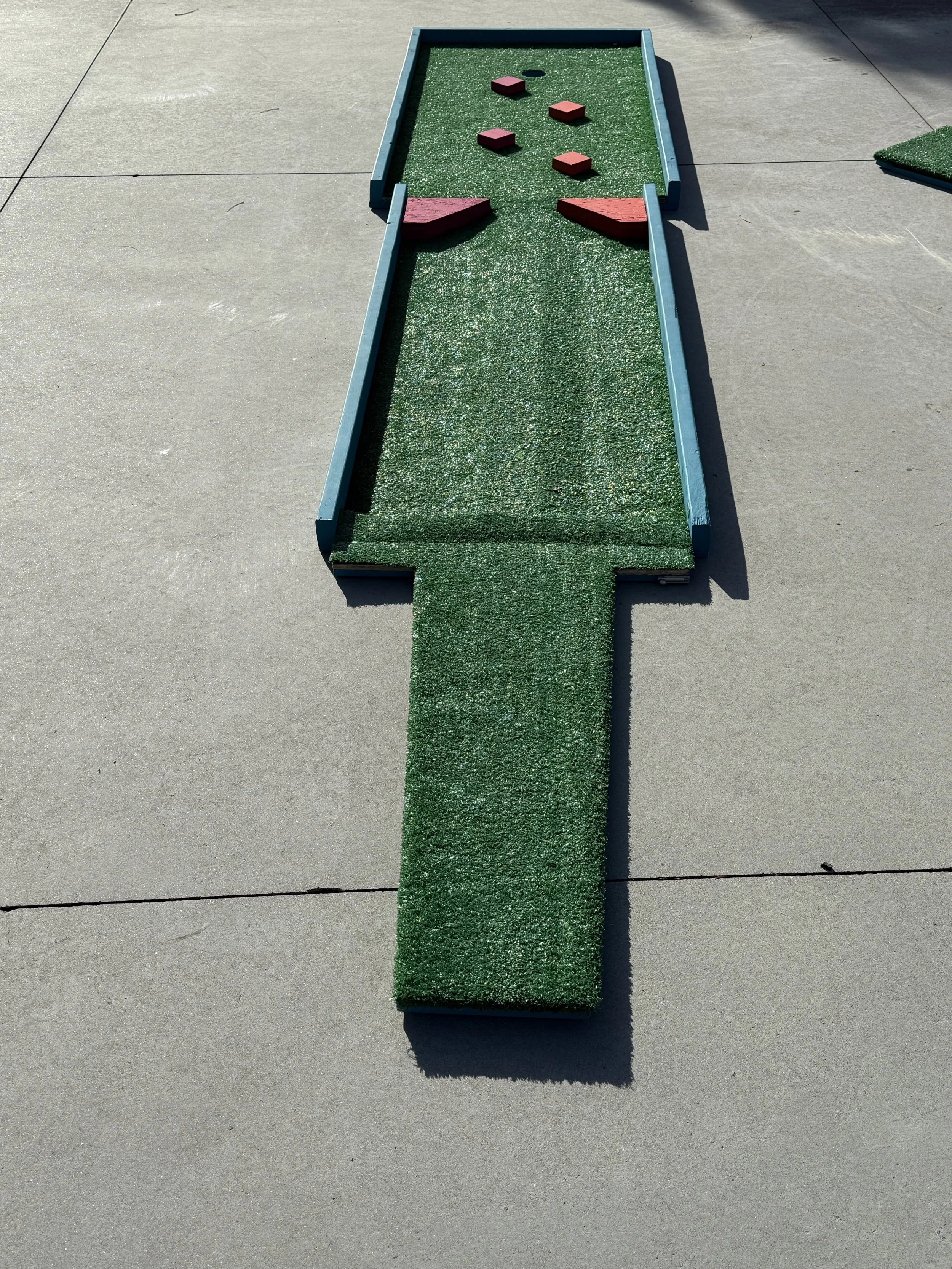 Miniature golf putting green with obstacles on a concrete sidewalk.