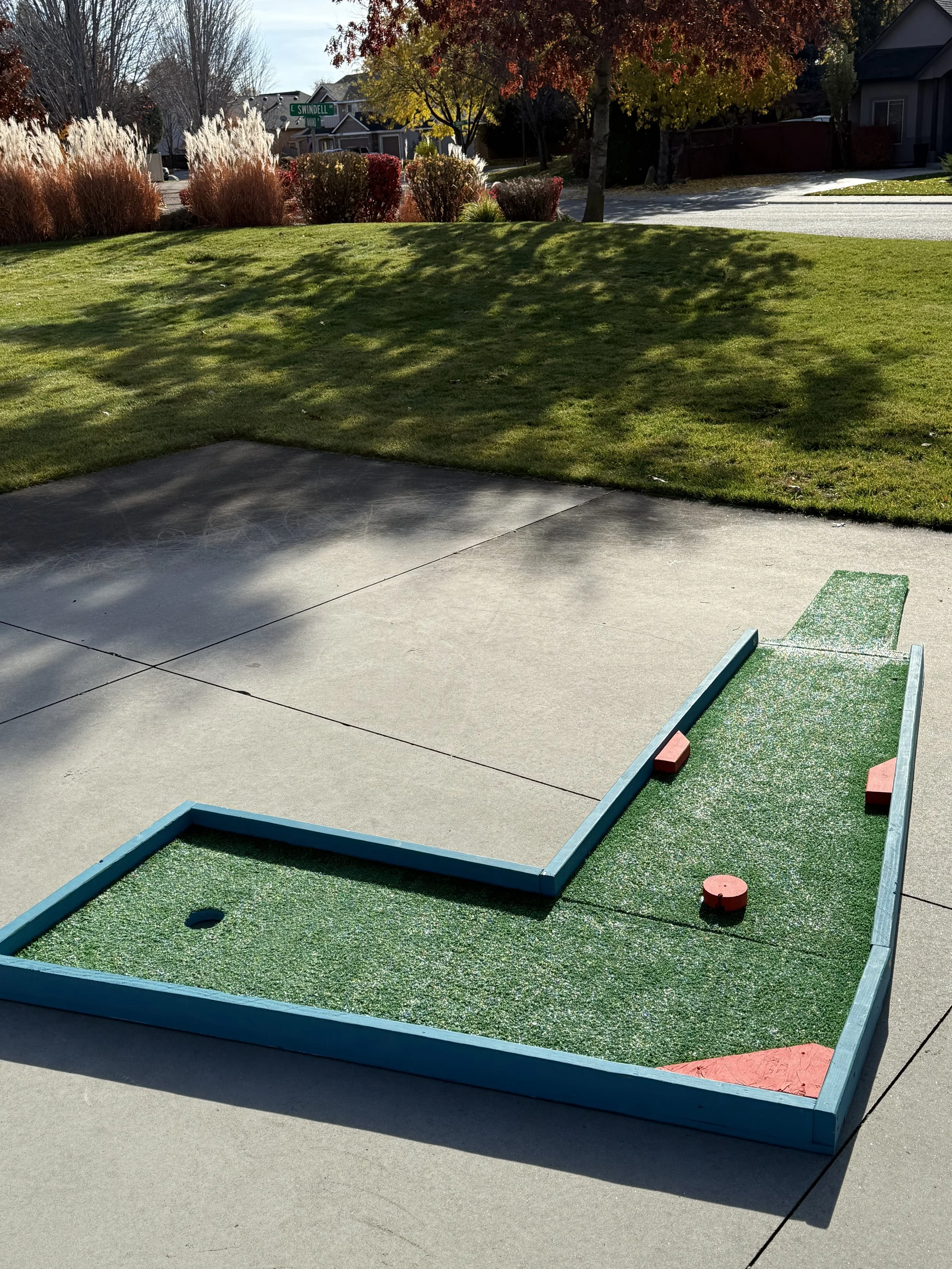 Miniature golf course putting green with three red obstacles on a concrete patio