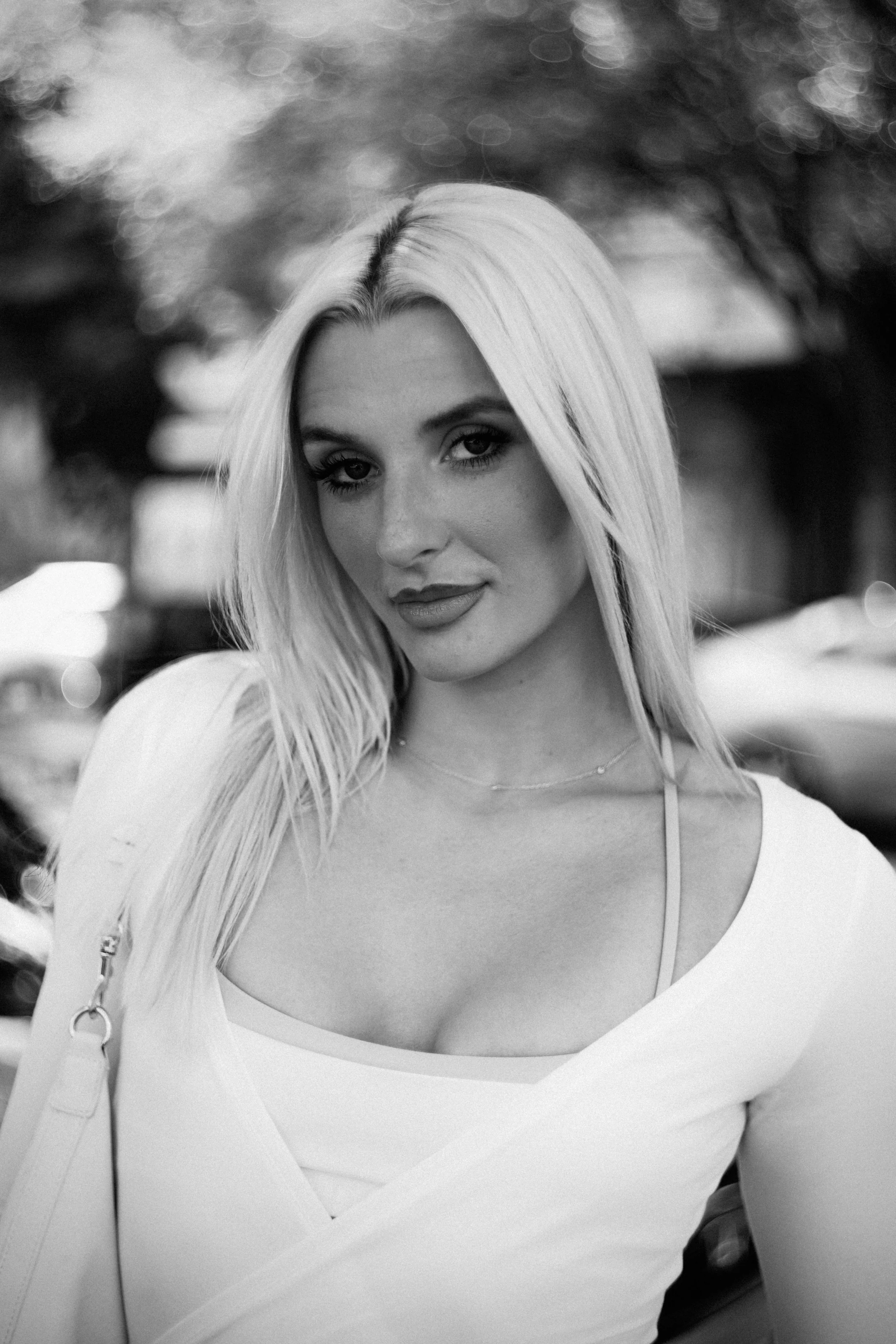 Black and white photo of a woman with long blonde hair, looking at the camera, with a blurred background.