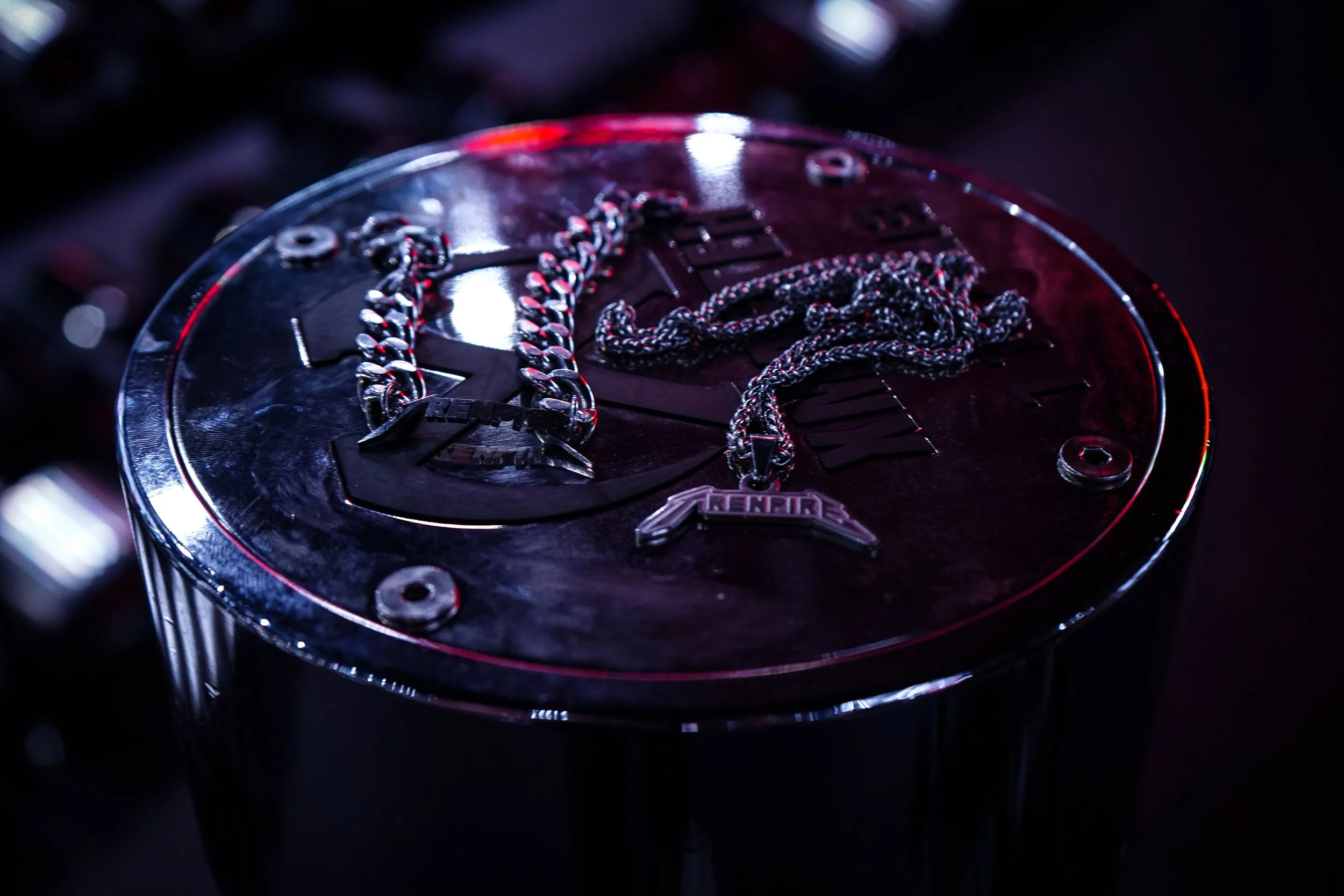 A round, metallic table with a Pepsi logo on top, displaying silver chains with pendants and a black and silver chain necklace, with chips of light reflecting off the surface.