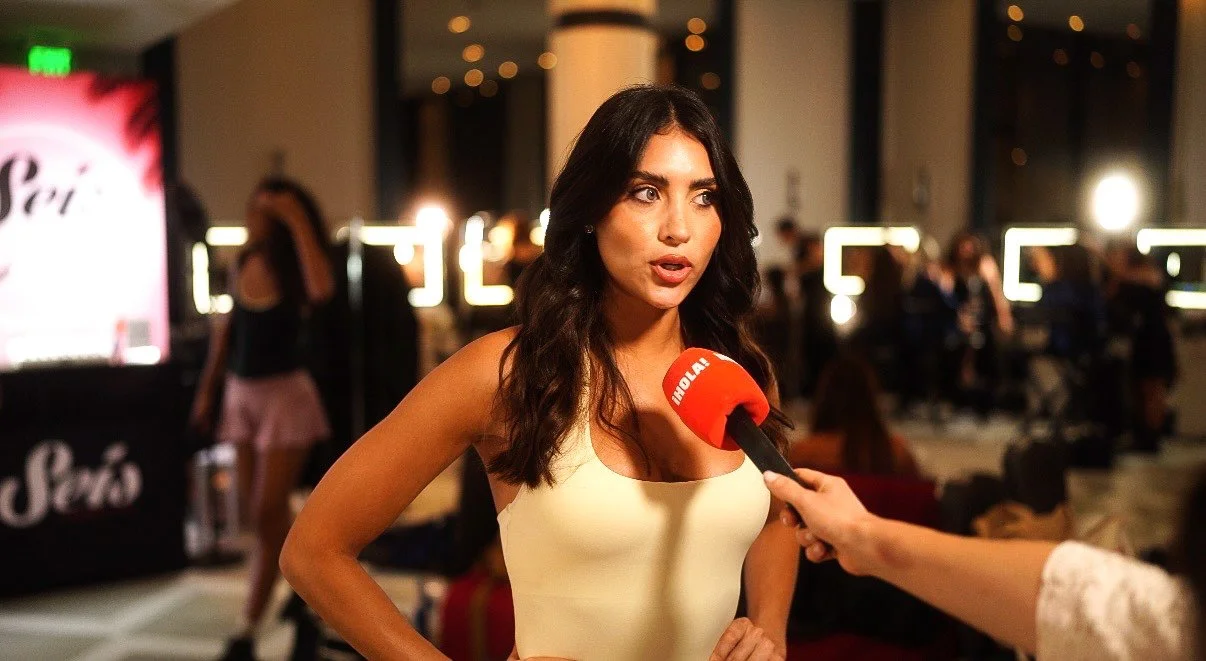 Woman being interviewed with a red microphone in the glam room of Miami Swim Week: The Shows.
