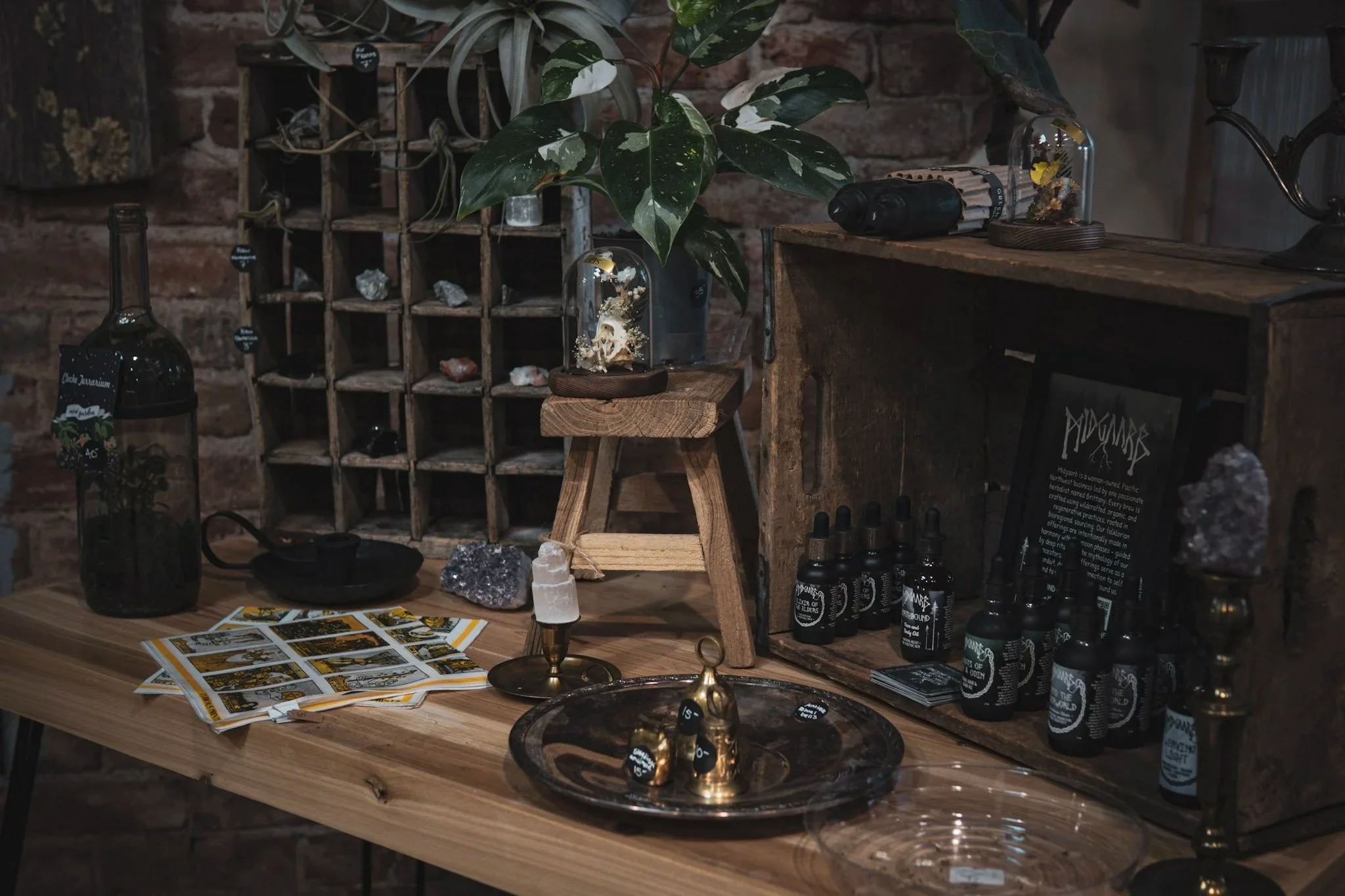 A tabletop display featuring various items such as bottles, candles, rocks, and a plant, with a brick wall background.