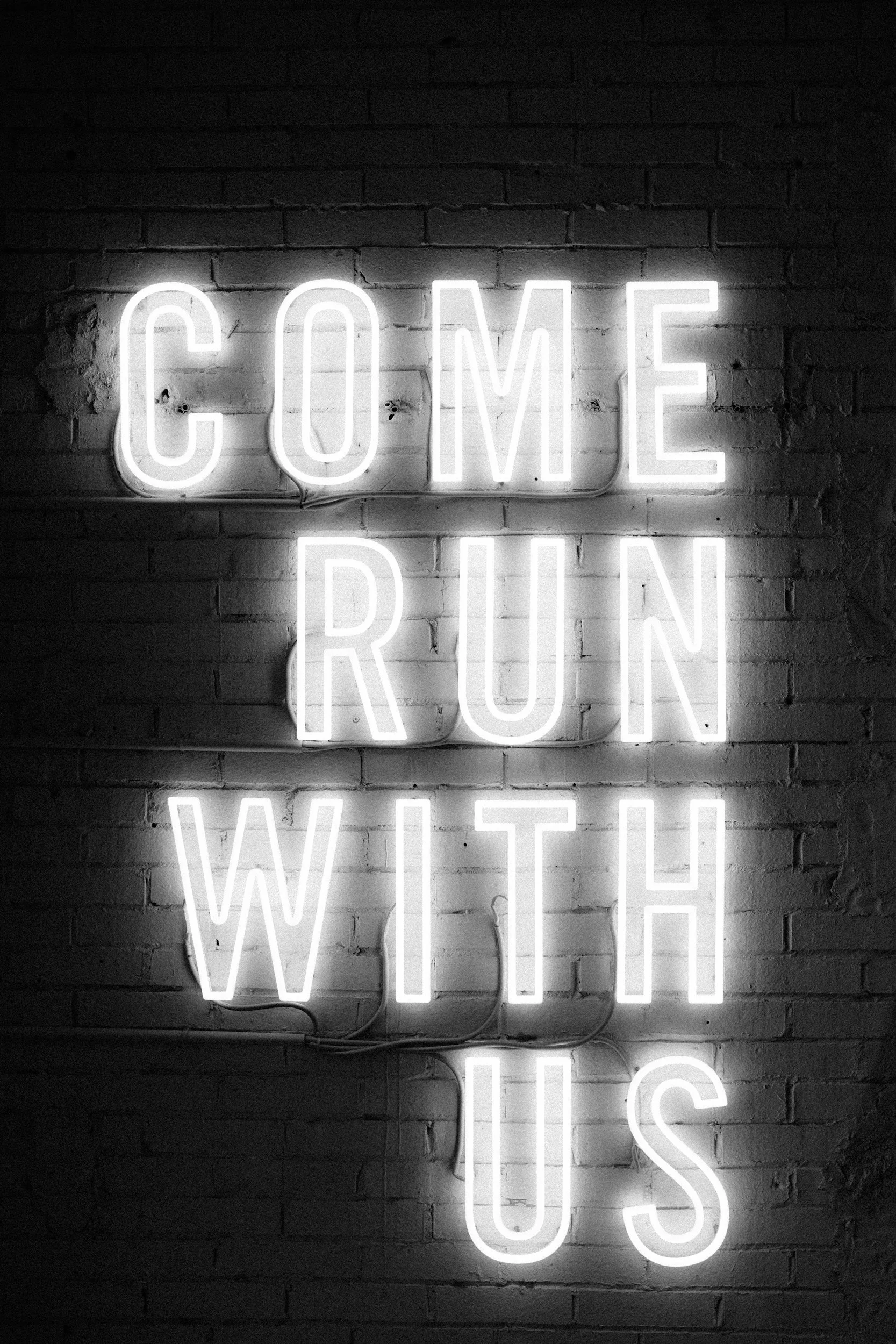 Neon sign on a brick wall that reads 'COME RUN WITH US'.