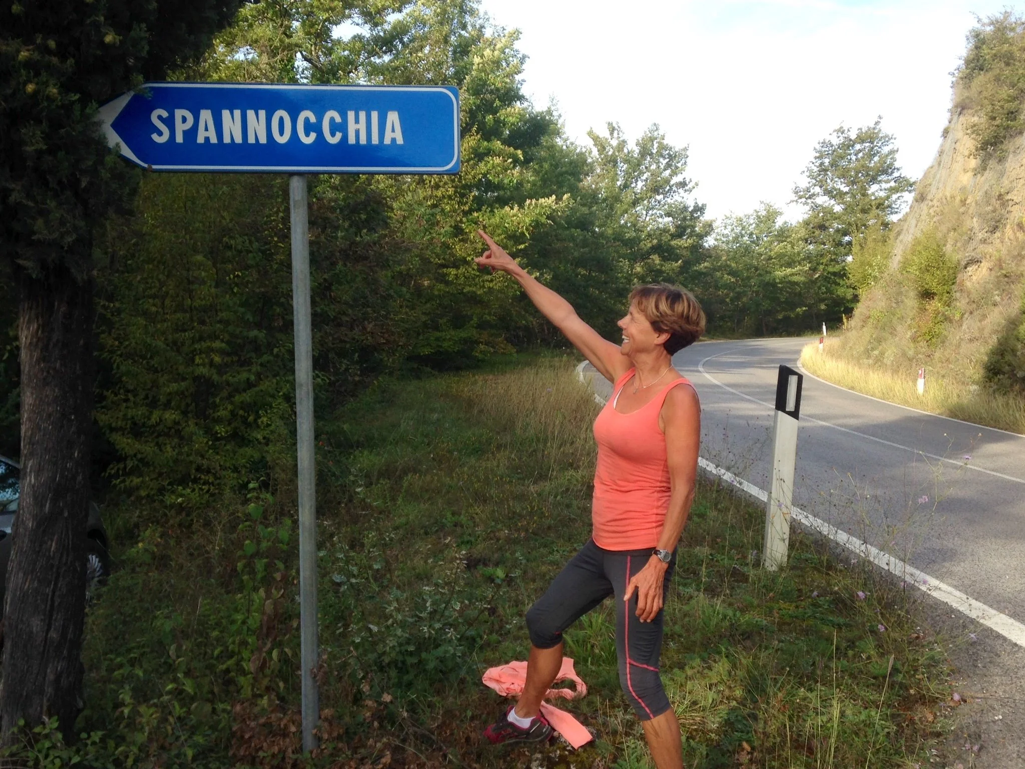 Smiling middle-aged woman with short brown hair, wearing glasses and a white button-up shirt, against a plain white background.