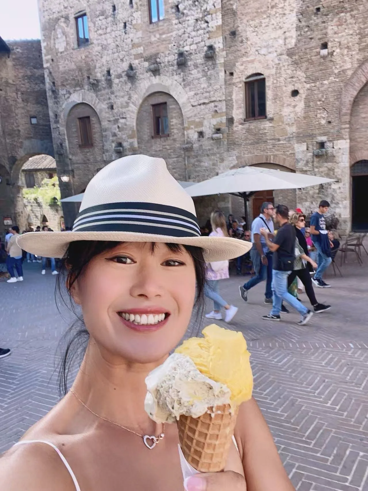 A woman with long black hair wearing a white blouse, smiling against a plain white background.
