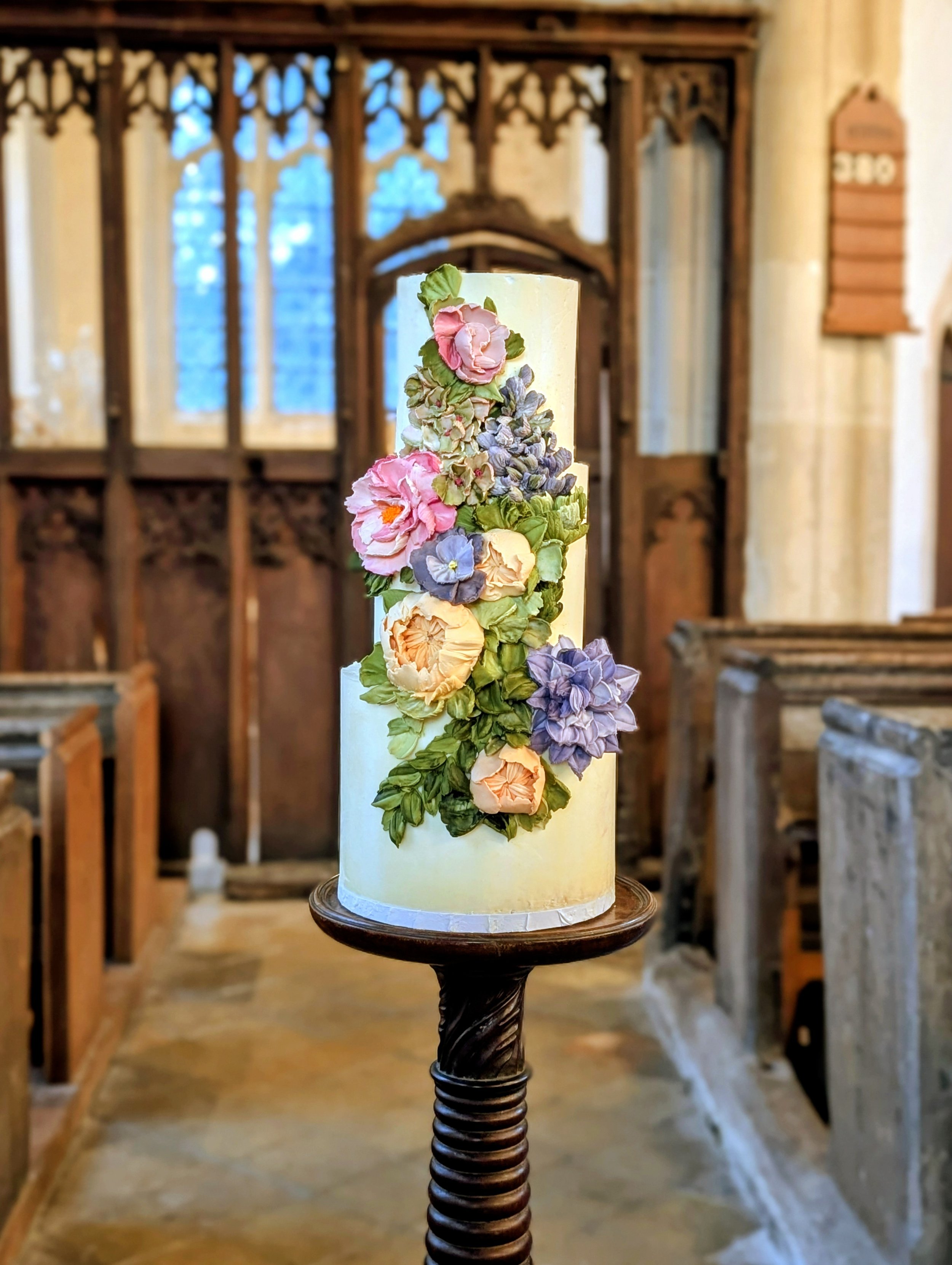 A white three-tier wedding cake featuring luxury hand-sculpted white chocolate botanicals.