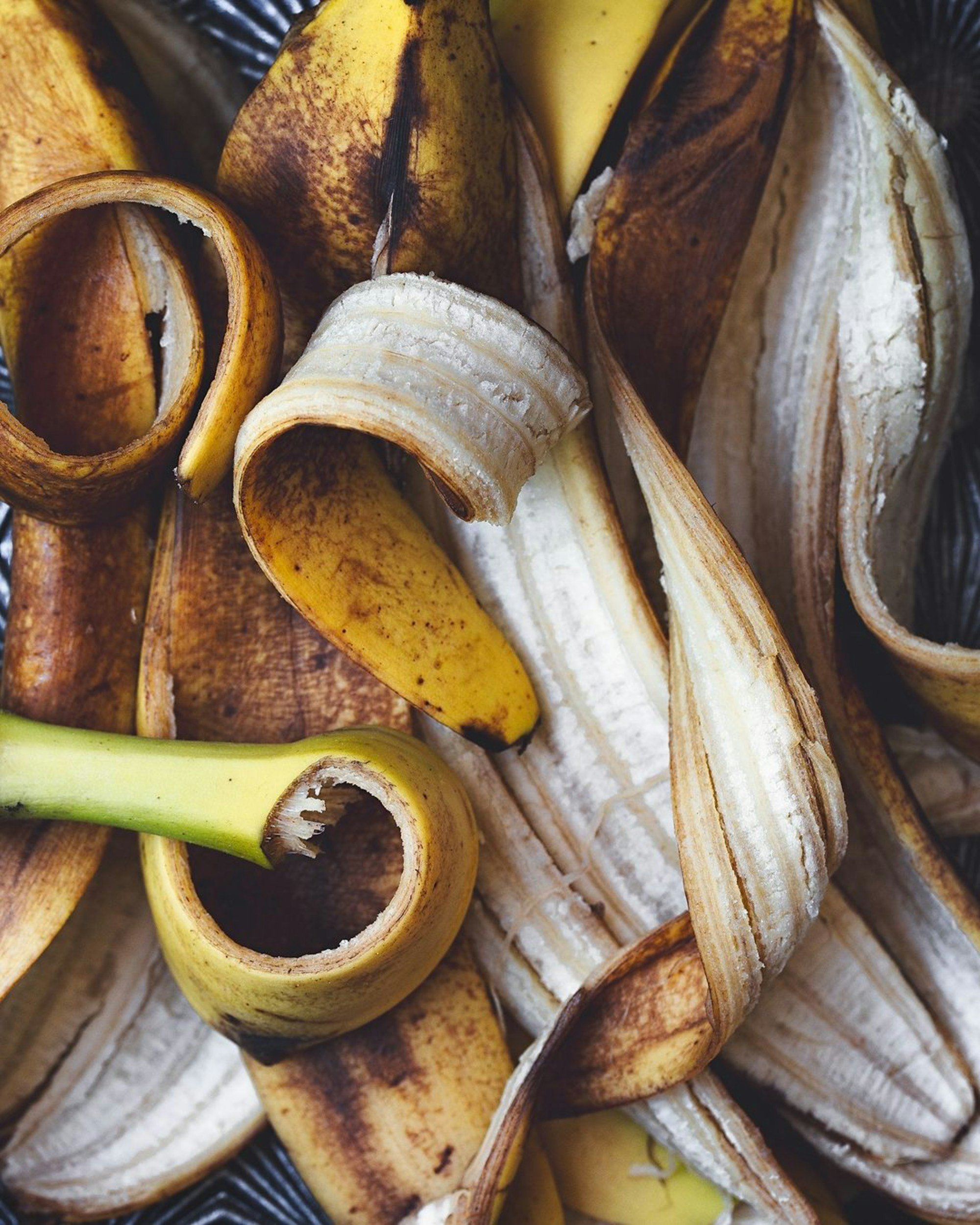 Close-up of banana peels, some partially peeled, showing inner fruit, with yellow and brown outer skins.