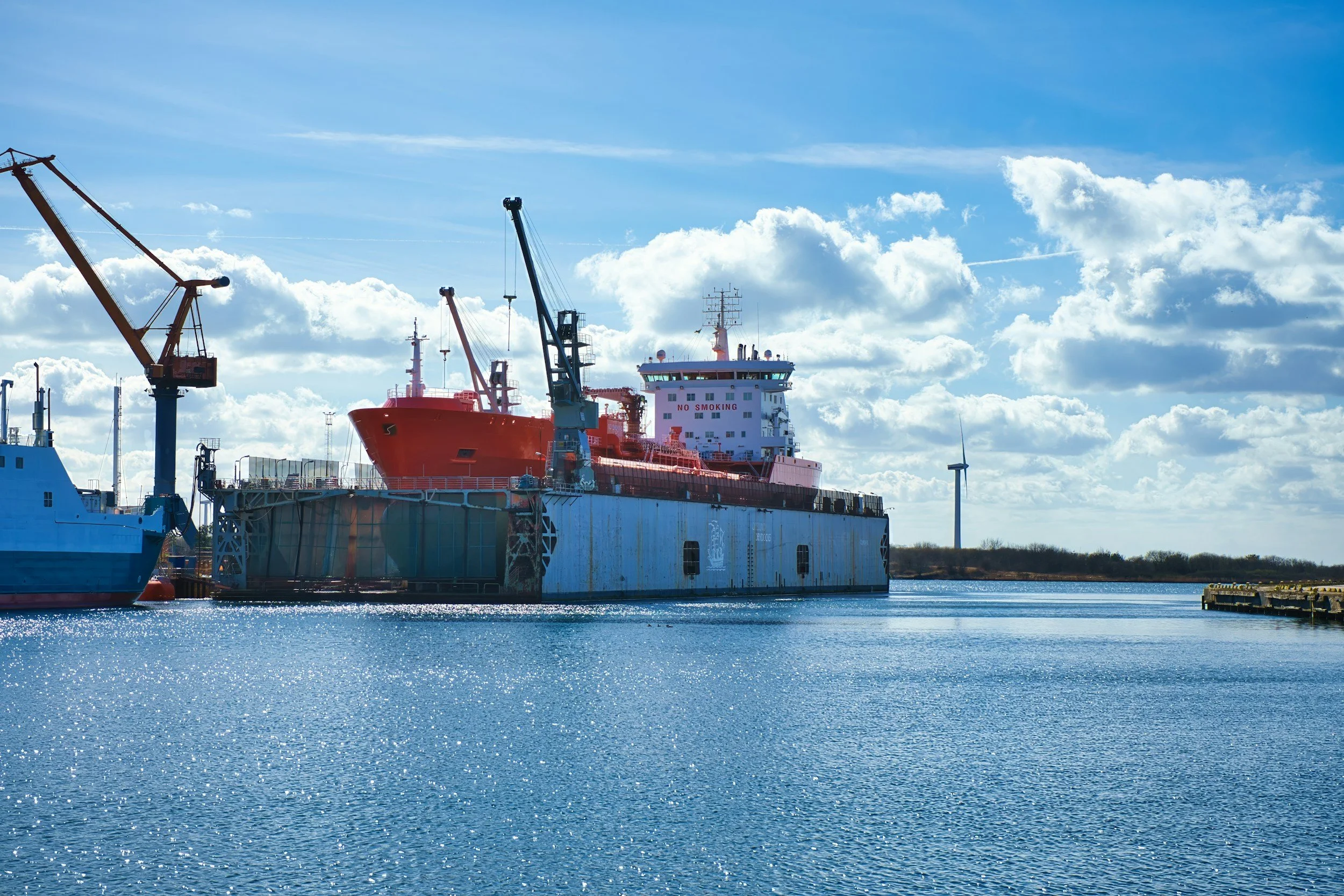 Large red ship docked at a harbor with blue water and a partly cloudy sky in the background.