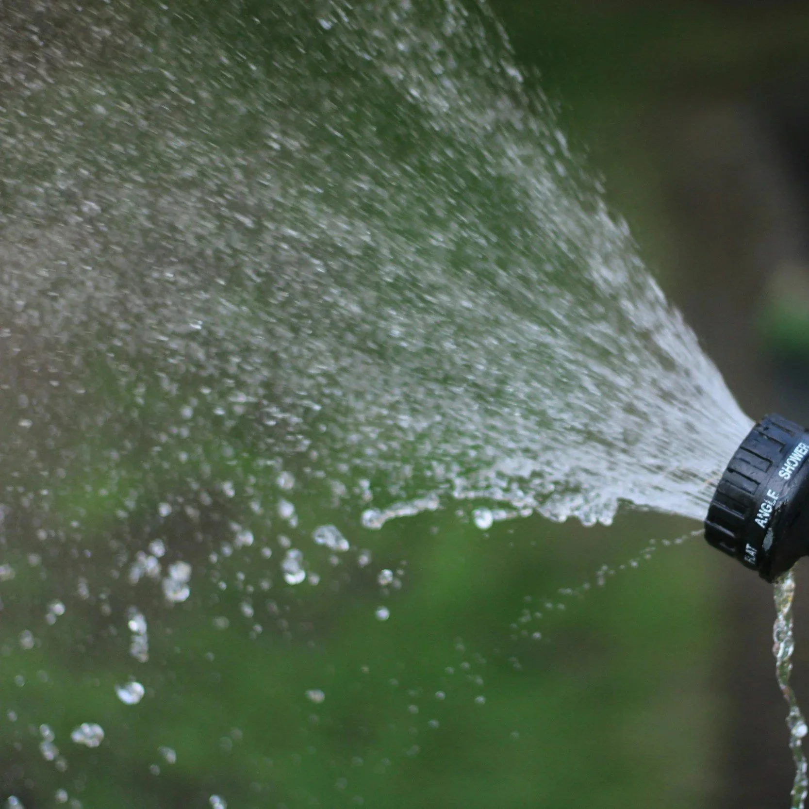 Water spray from a garden hose nozzle with green background