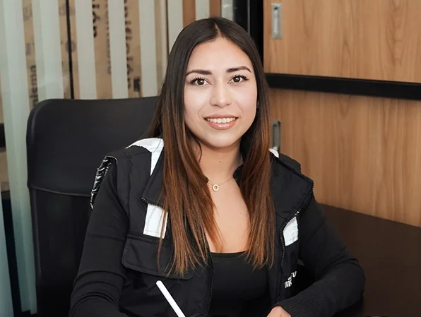 Mujer sonriendo, sentada en una mesa en un entorno de oficina.