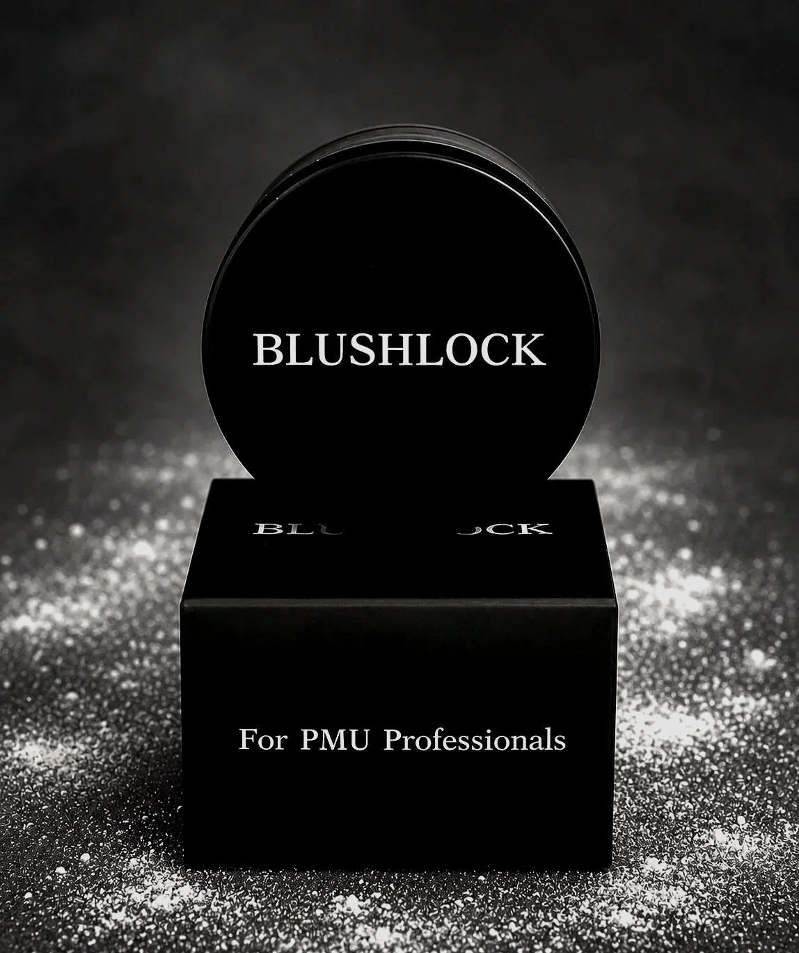 Black container with the text "BLUSHLOCK" on top, placed on a black base with the words "For PMU Professionals" written on it. The background is dark with a sparkling, glittery surface.