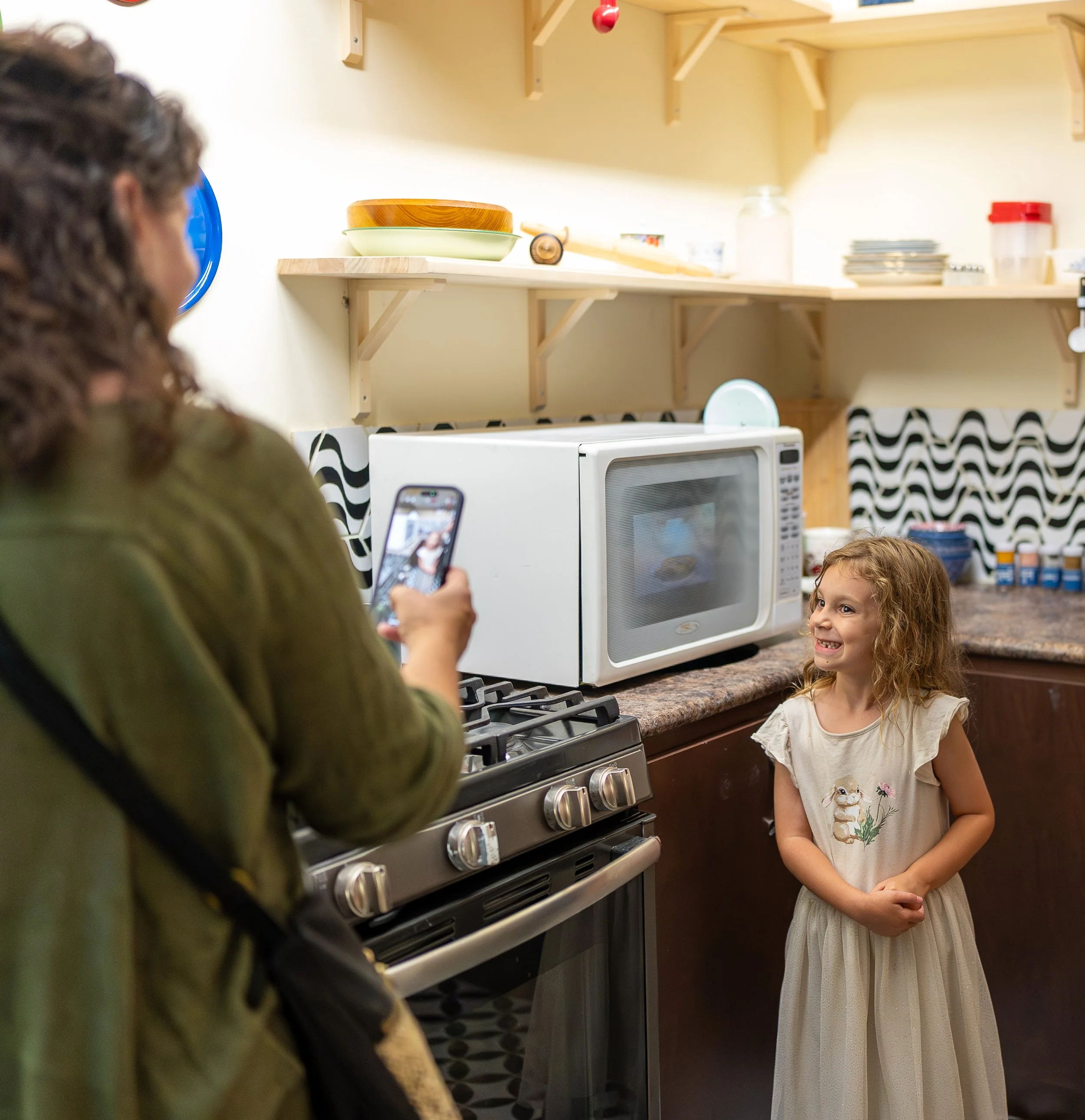 A woman taking a picture of a girl in the kitchen