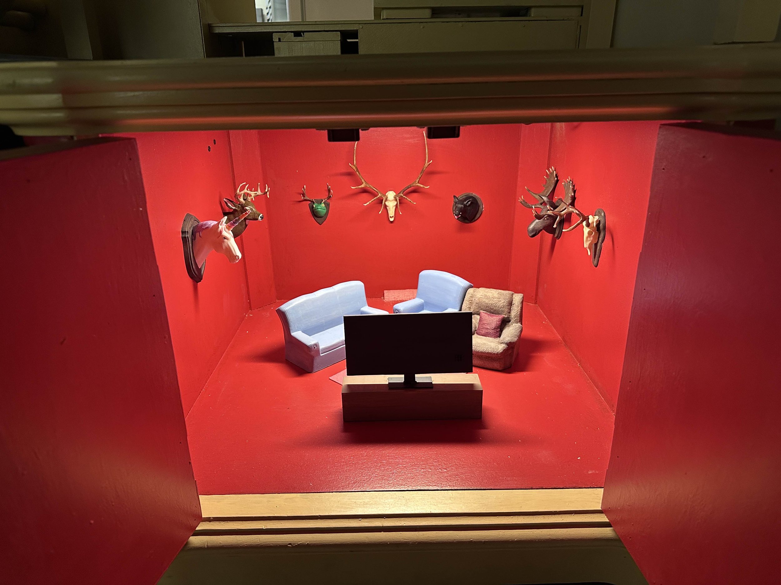 A small red compartment with miniature front room furniture and animal heads hanging on the wall.
