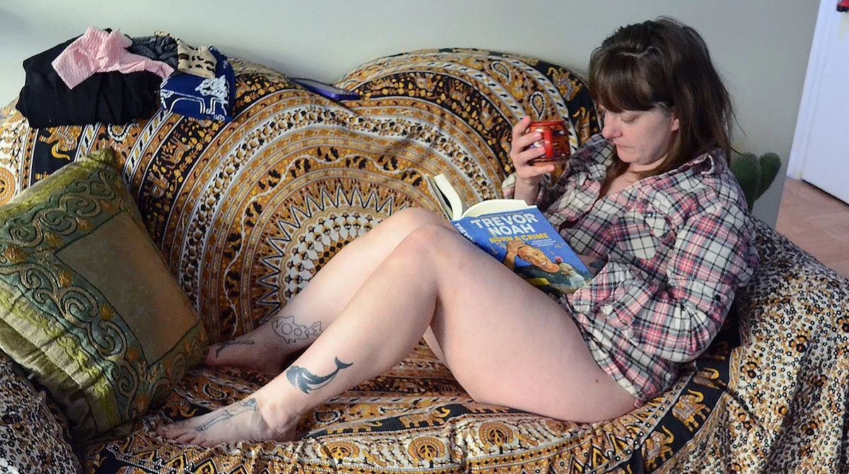 Lucy Dee drinking coffee and reading a book on the couch