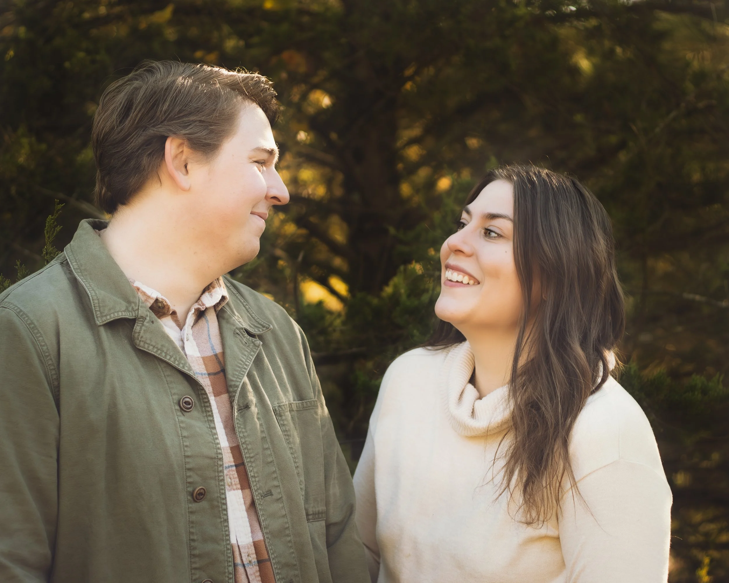 A young man and woman smiling at each other outdoors during autumn.