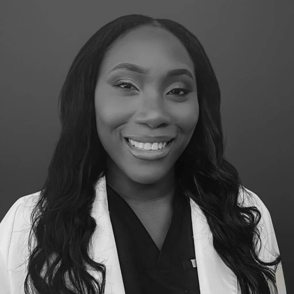 Black and white portrait of a smiling woman with long wavy hair, wearing a white coat over a dark shirt.