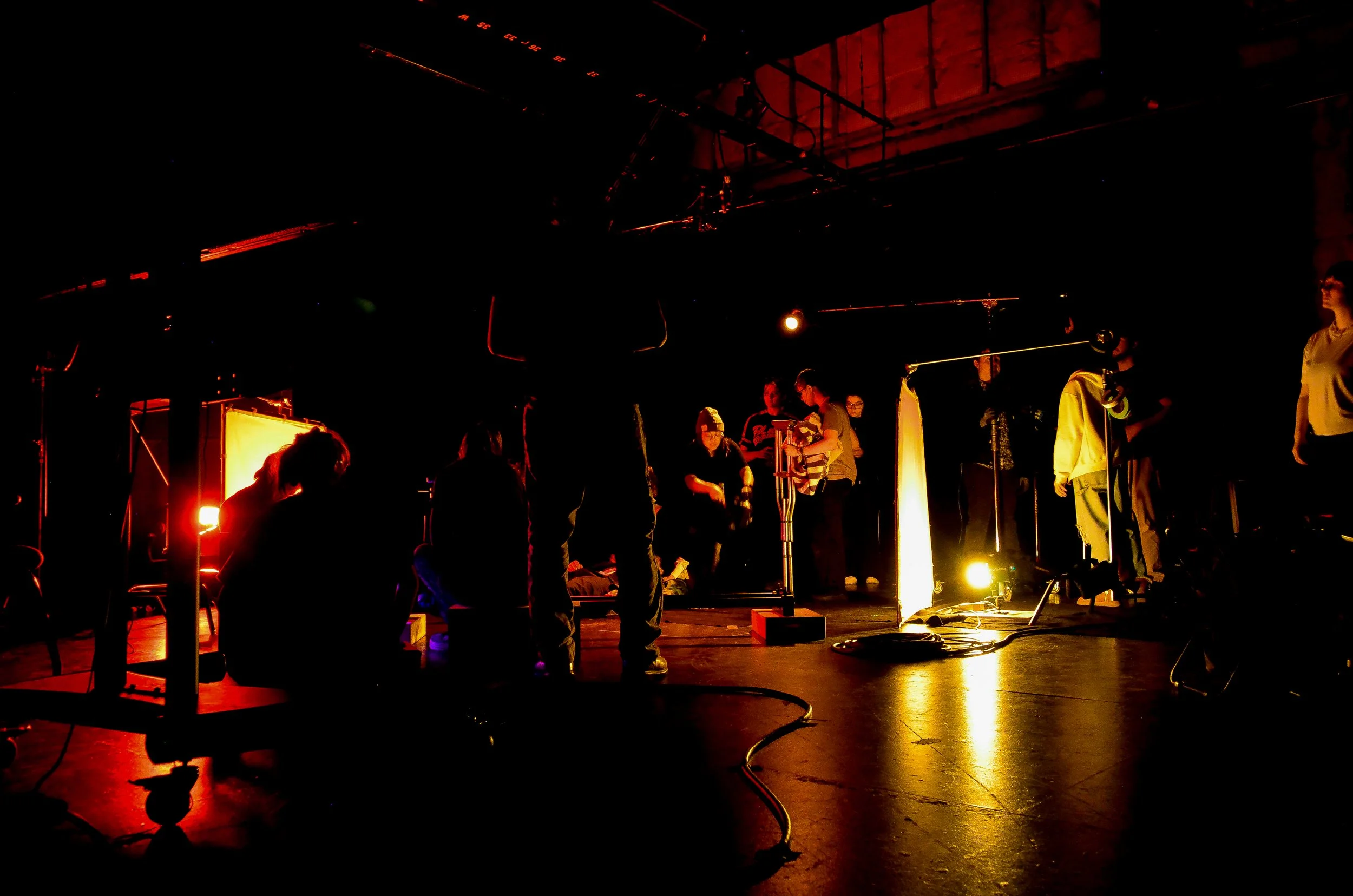 People setting up or rehearsing on a dimly lit stage with stage lights and equipment.