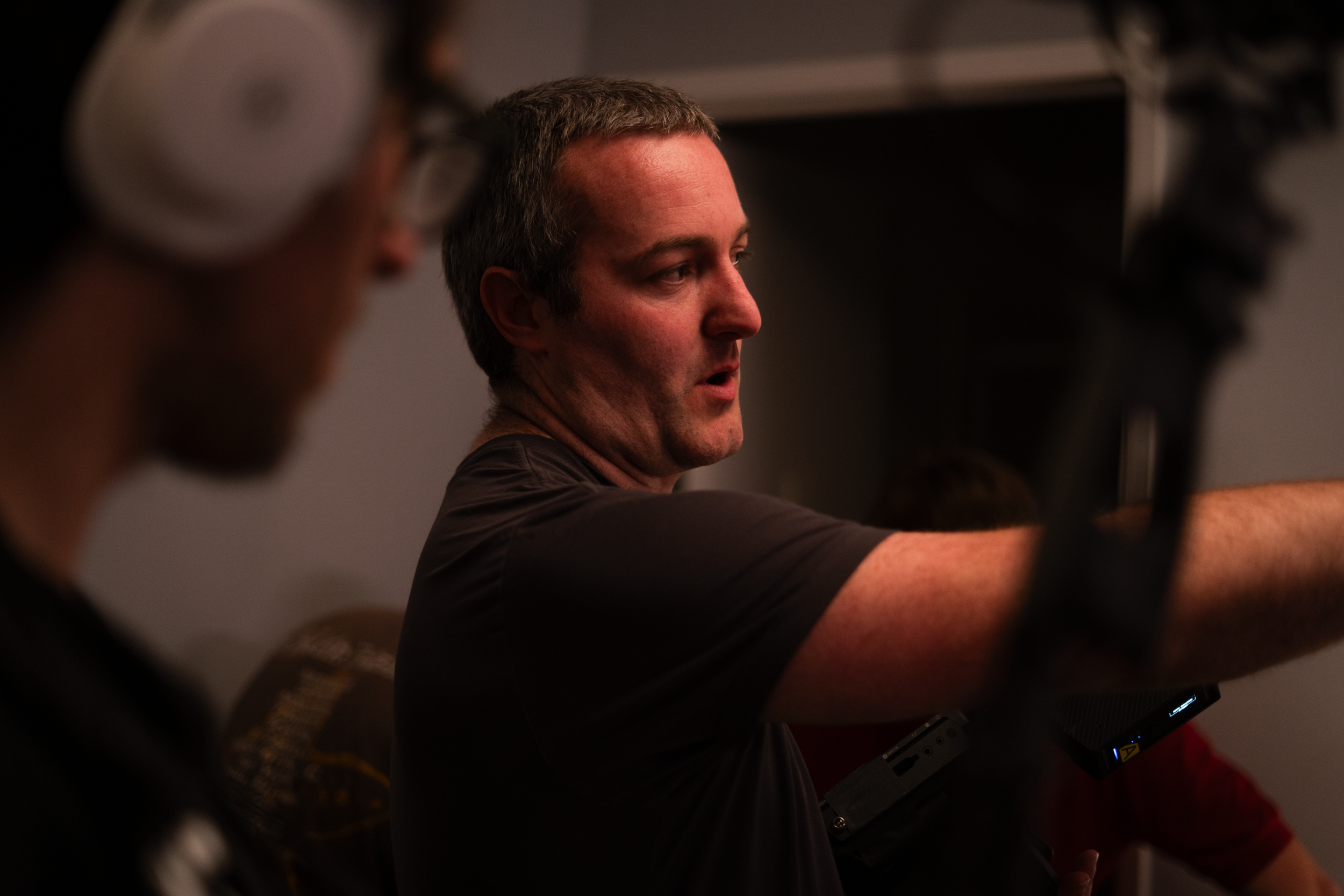 A man extending his arm forward, engaged in a discussion or presentation, with another person blurred in the foreground.