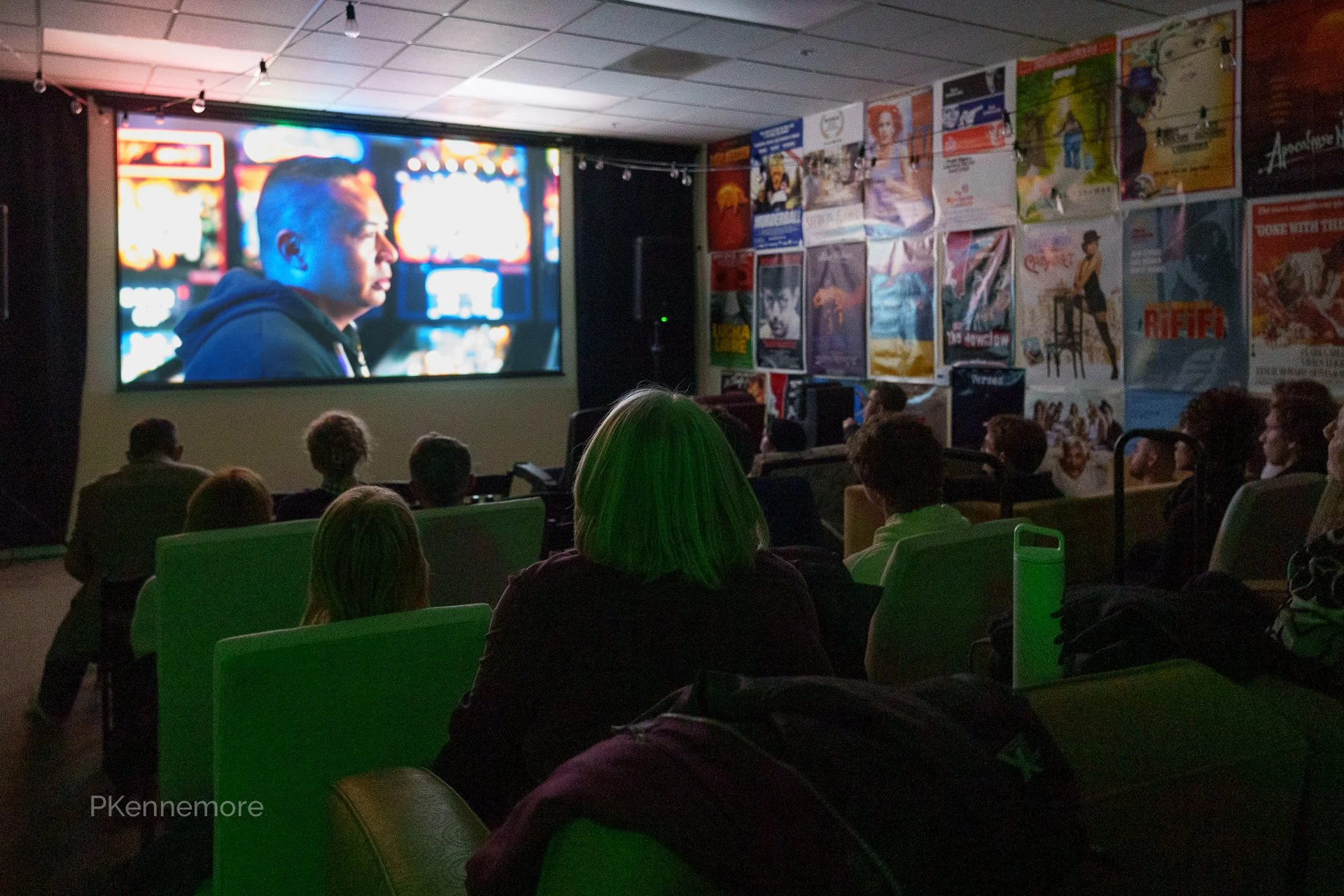 People watching a movie in a dark theater with a large screen and colorful posters on the wall.