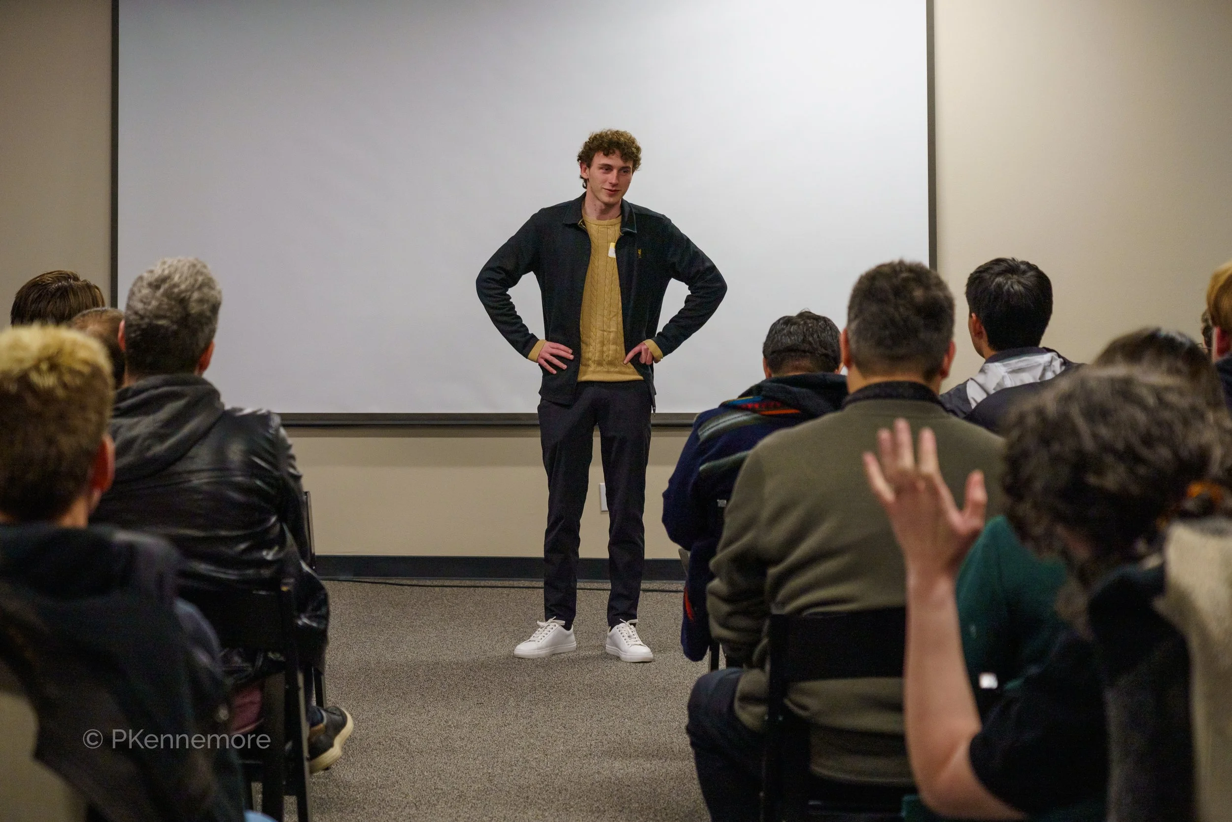 Young man standing in front of an audience during a presentation in a classroom or conference room.