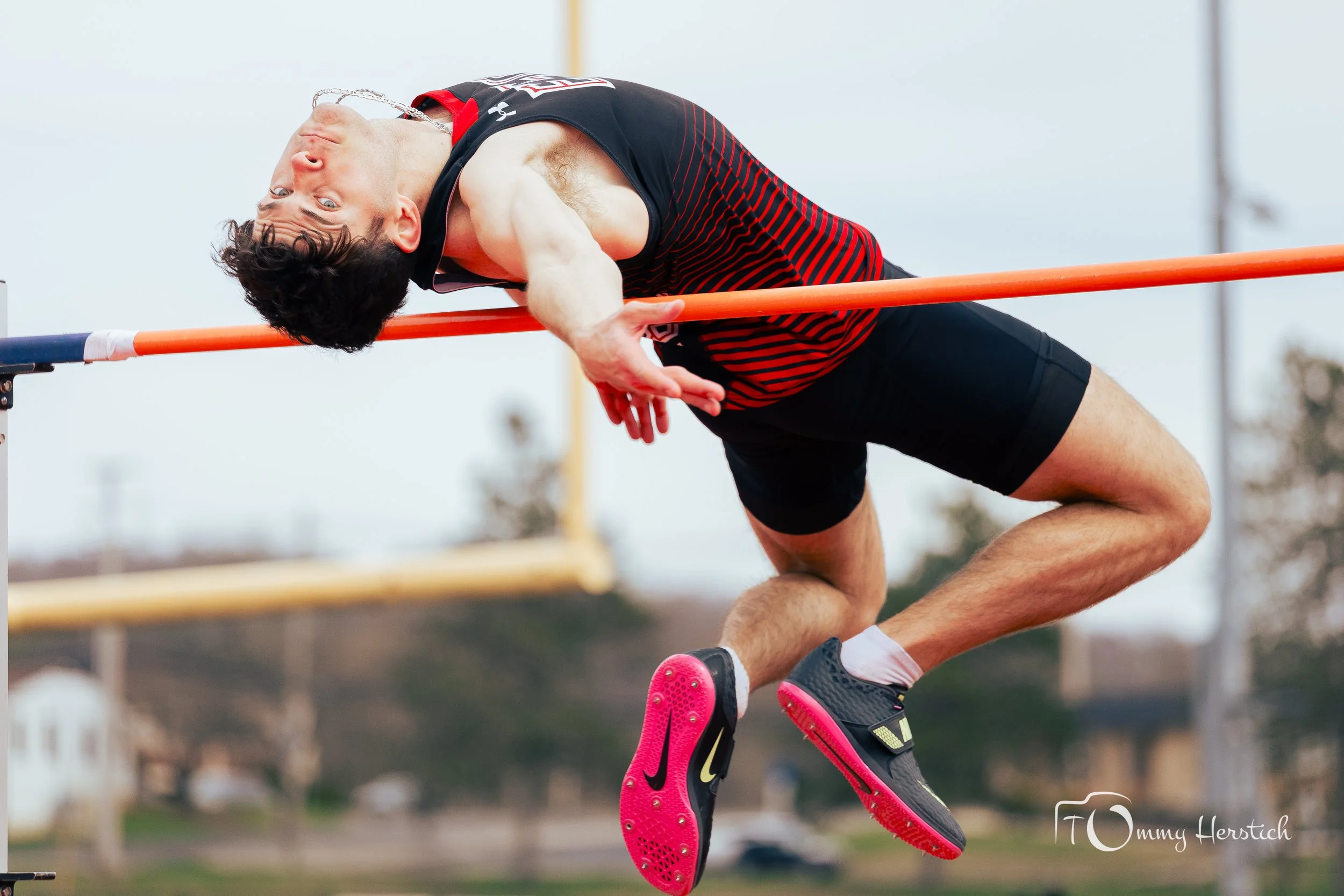 A male athlete in mid-air jumping over a high jump bar during a track and field event.