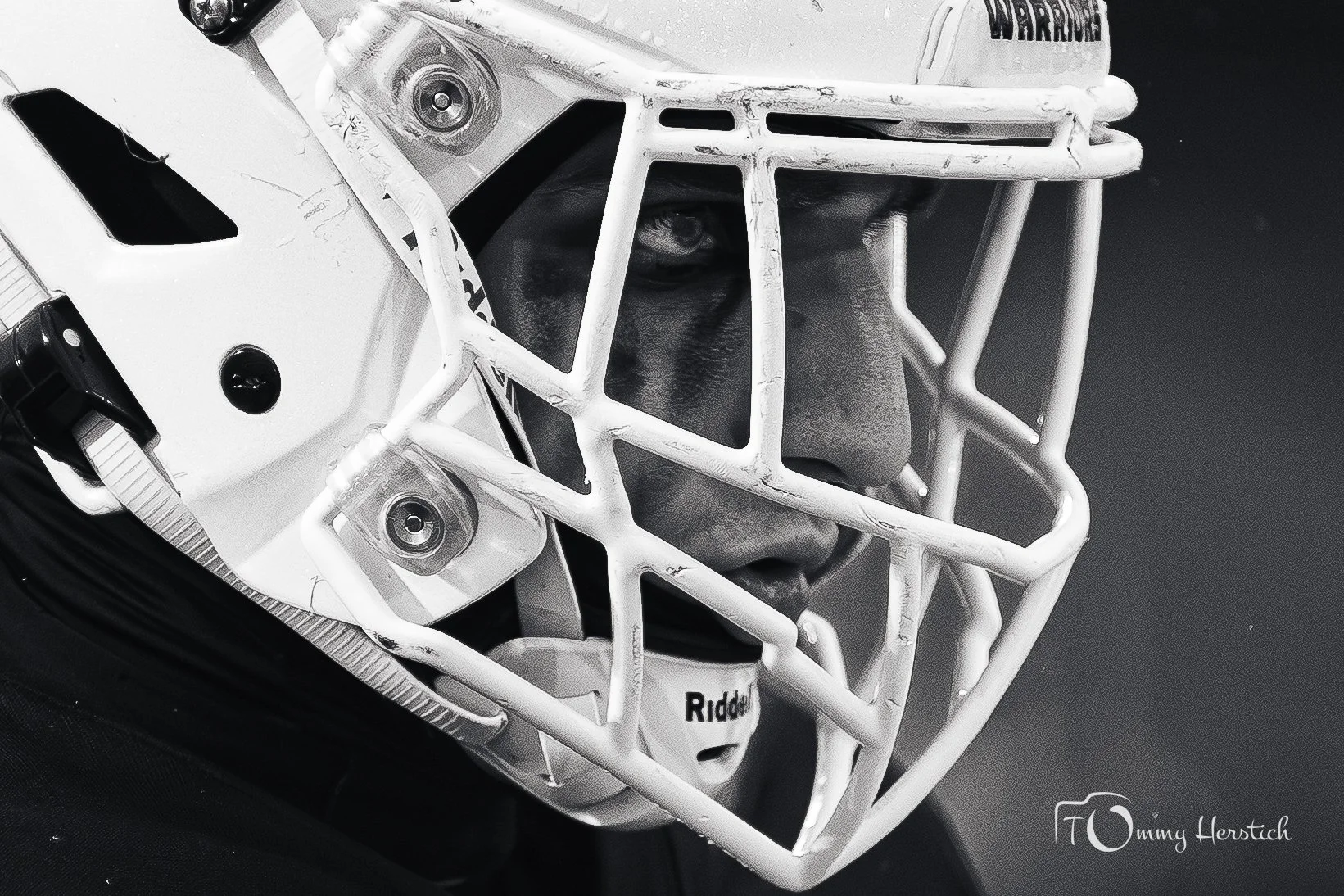 Close-up of a football helmet with a face mask, showing a person's face through the faceguard. The helmet is white with visible scratches.