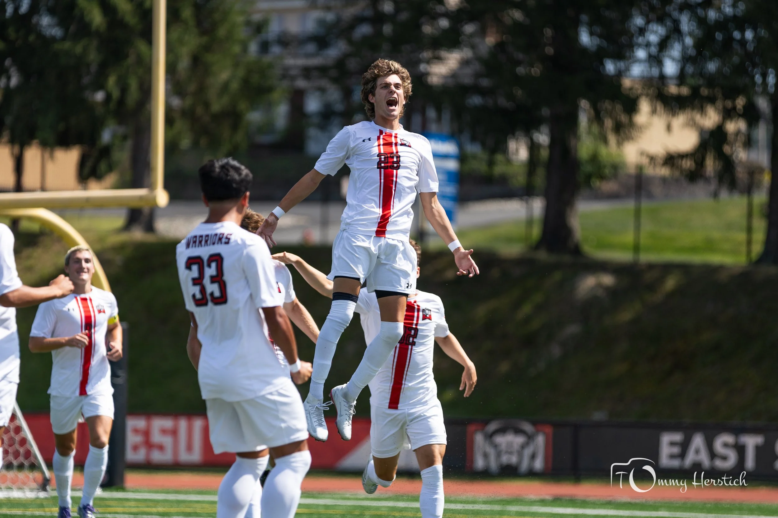 Soccer players celebrating on the field with one player jumping in the air and others surrounding him.