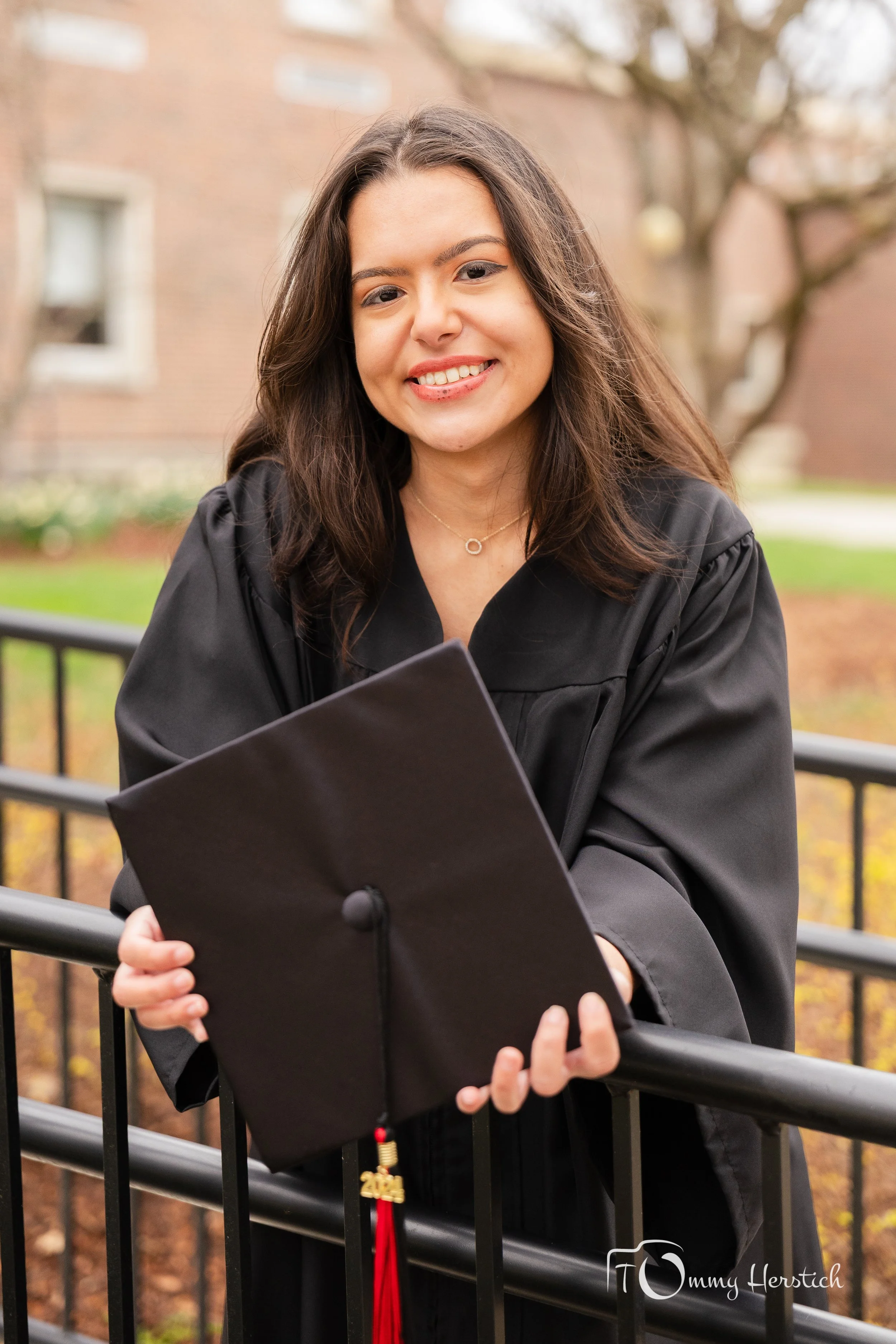 A young woman in a graduation cap and gown holding a diploma outside on a balcony