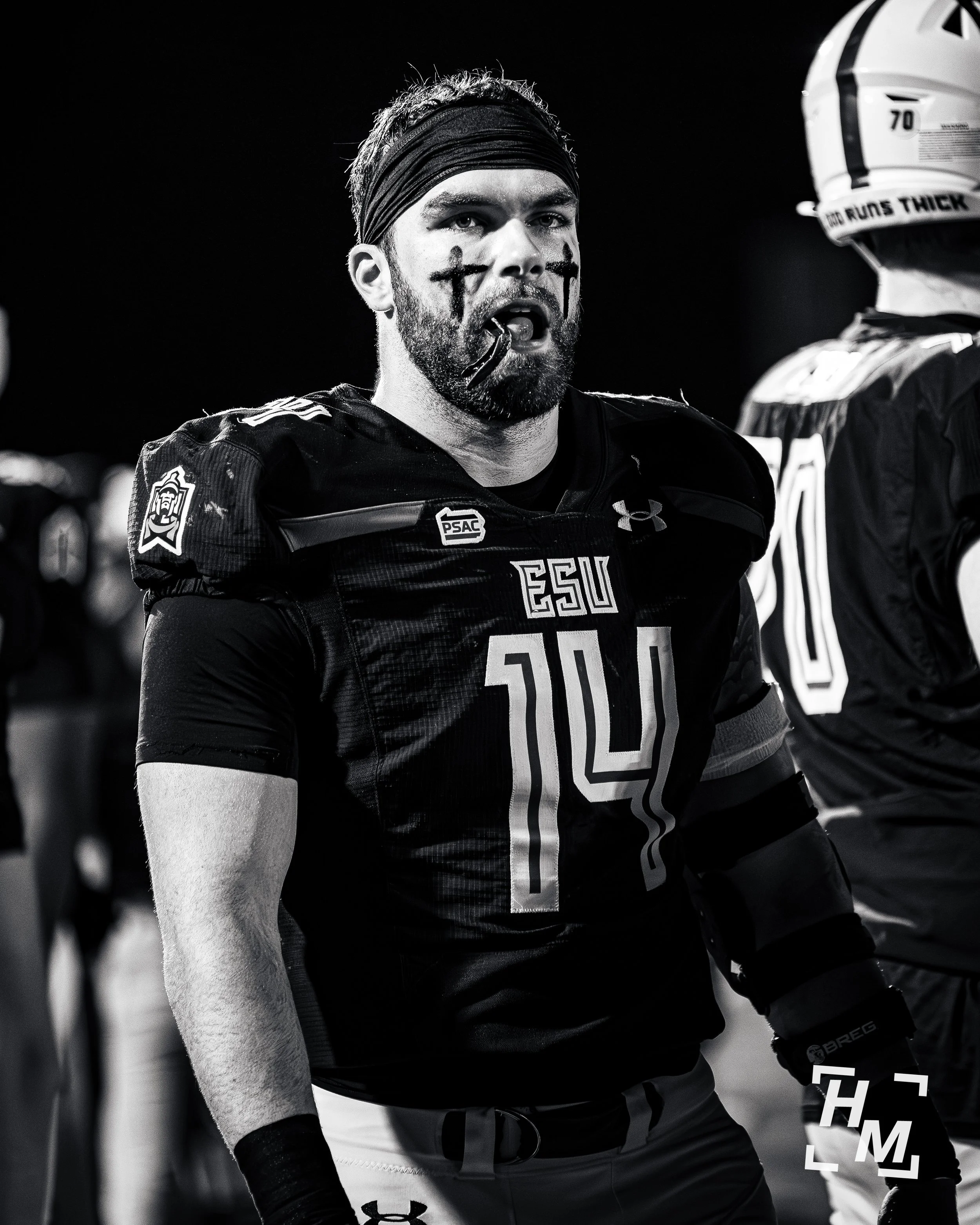 Black and white photo of a football player with face paint, wearing a jersey with the number 14, standing on the field.