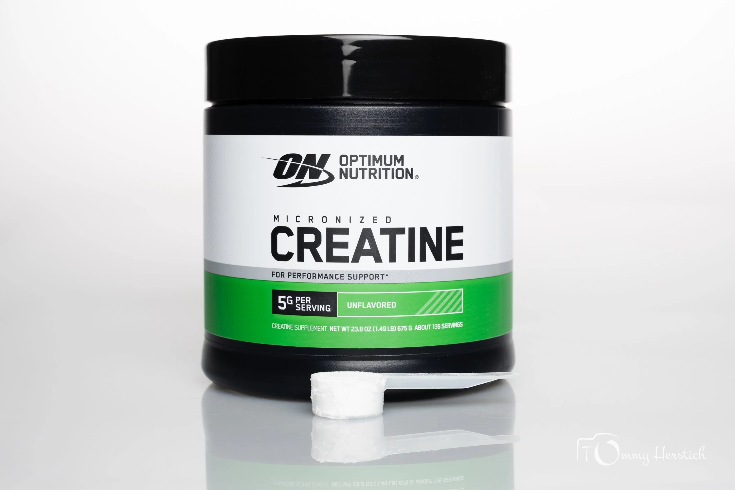 Container of Optimum Nutrition micronized creatine powder with a scoop in front of it on a white surface.