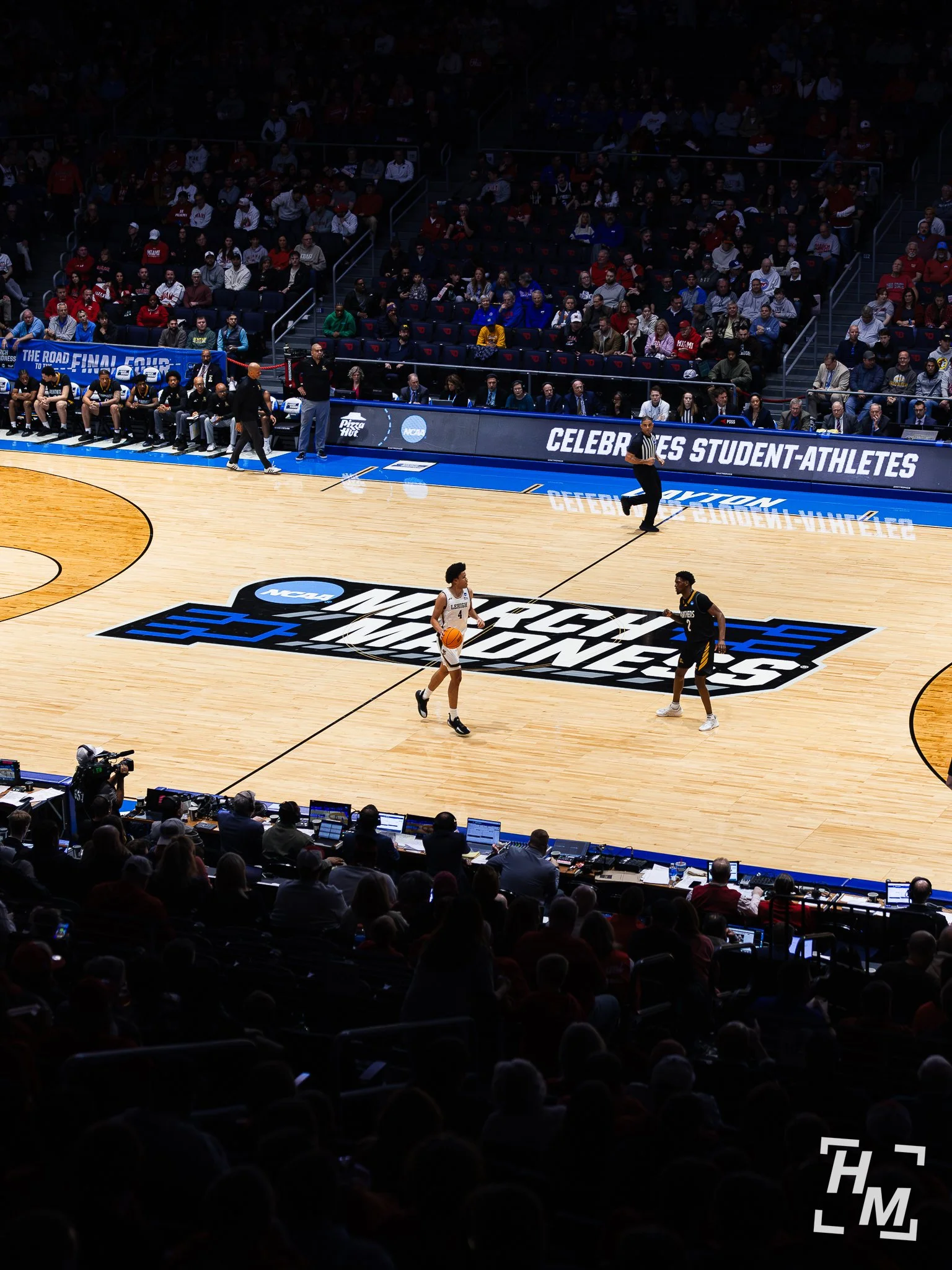 High angle basketball shot from stands looking down at two players standing on march madness logo