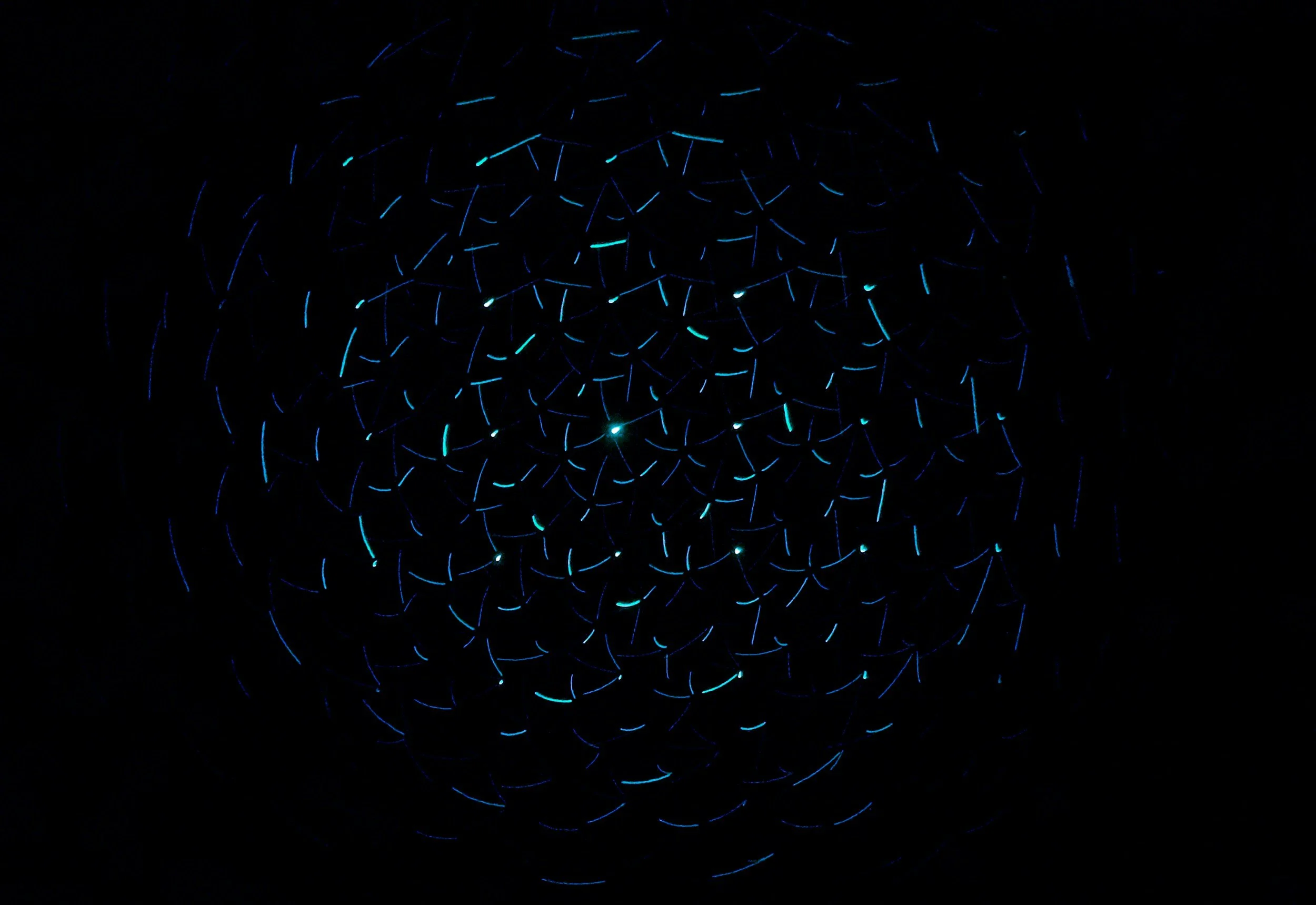 Light trails in shades of blue and cyan forming a spiral pattern against a black background.
