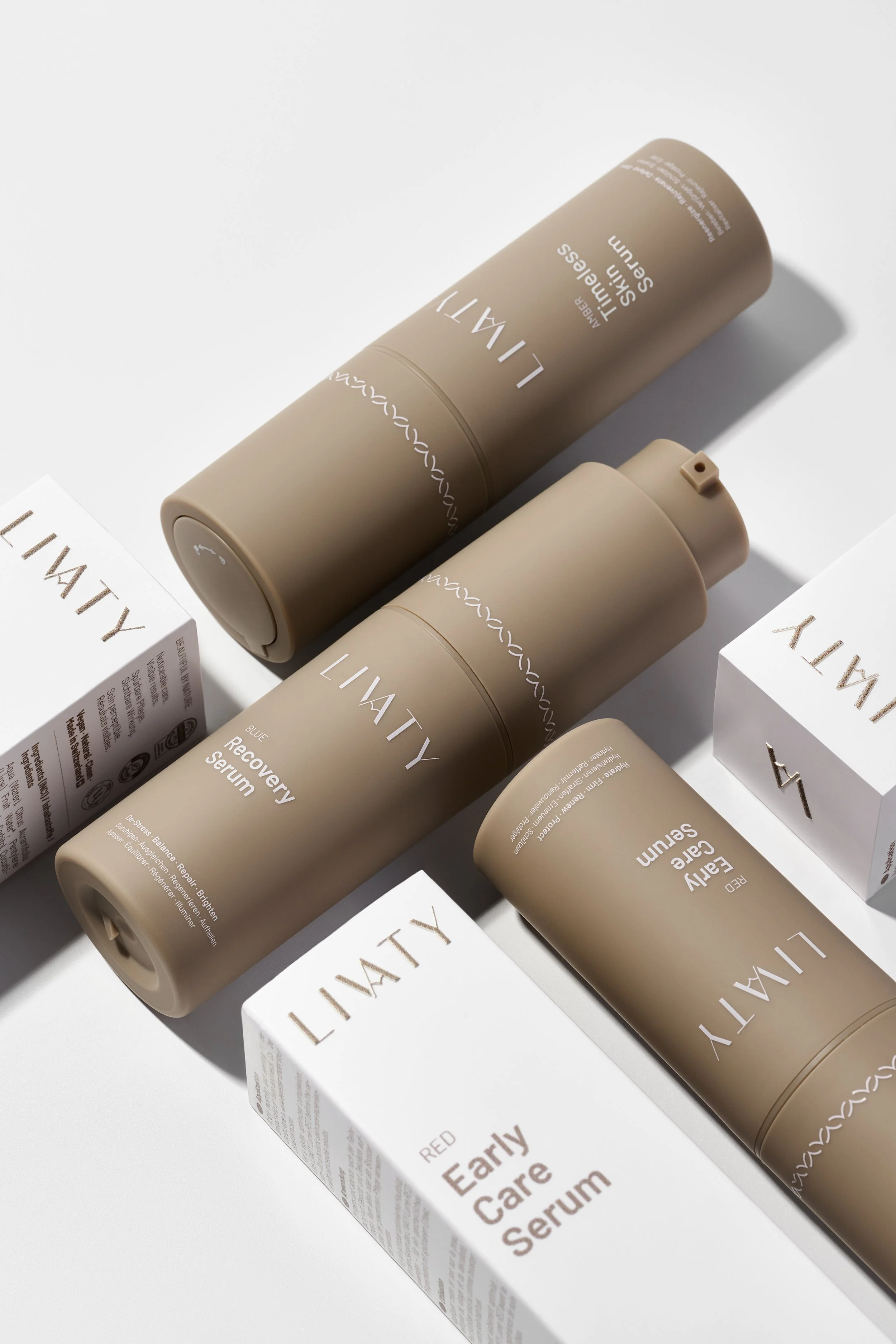 Arrangement of skincare products, including two beige bottles labeled 'LIVITY Recovery Serum' and 'LIVITY Early Care Serum,' and a white box labeled 'RED Early Care Serum,' on a white surface with soft shadows.