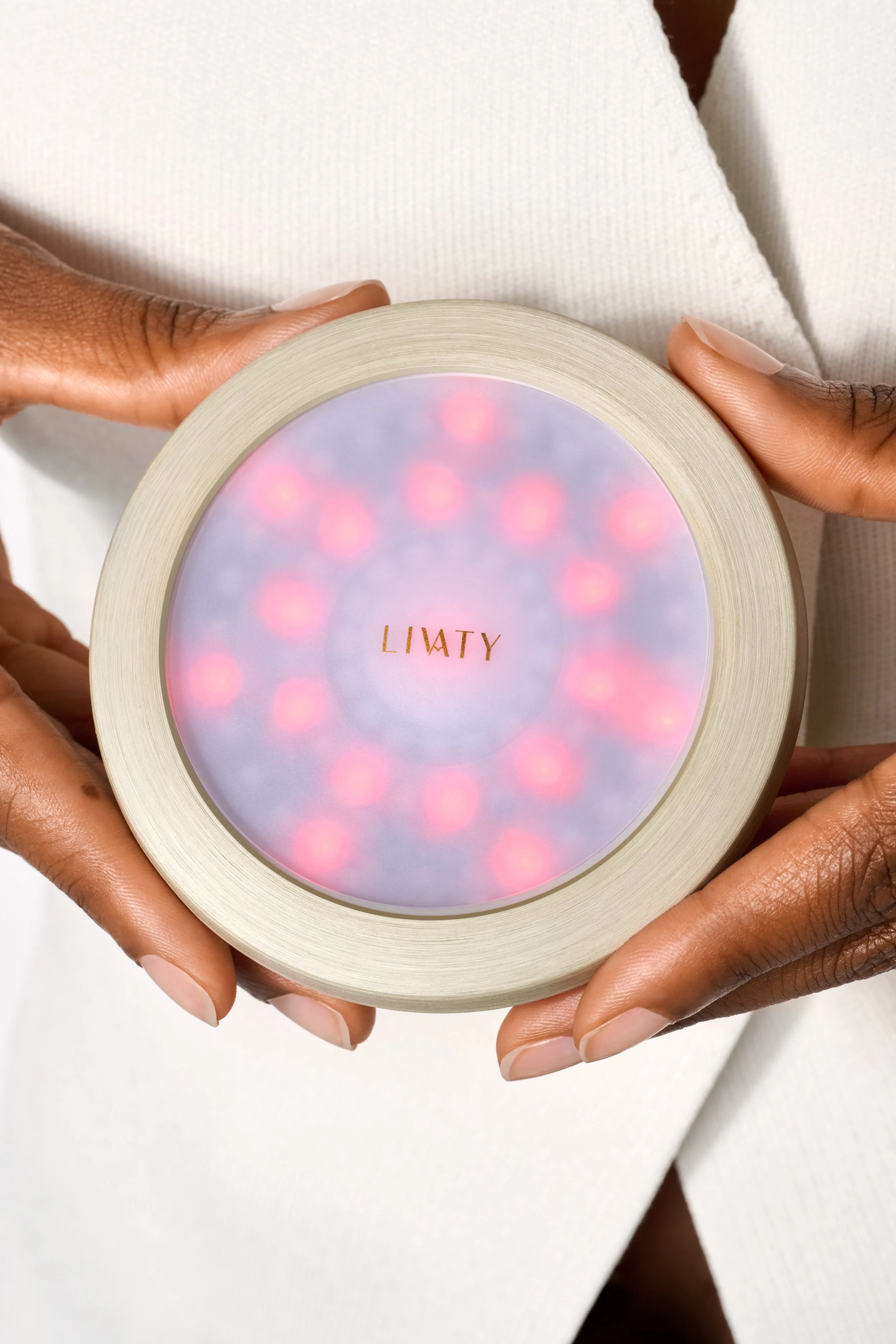Person holding a round, white container with a colorful, illuminated lid that says 'LILATY' in gold letters.