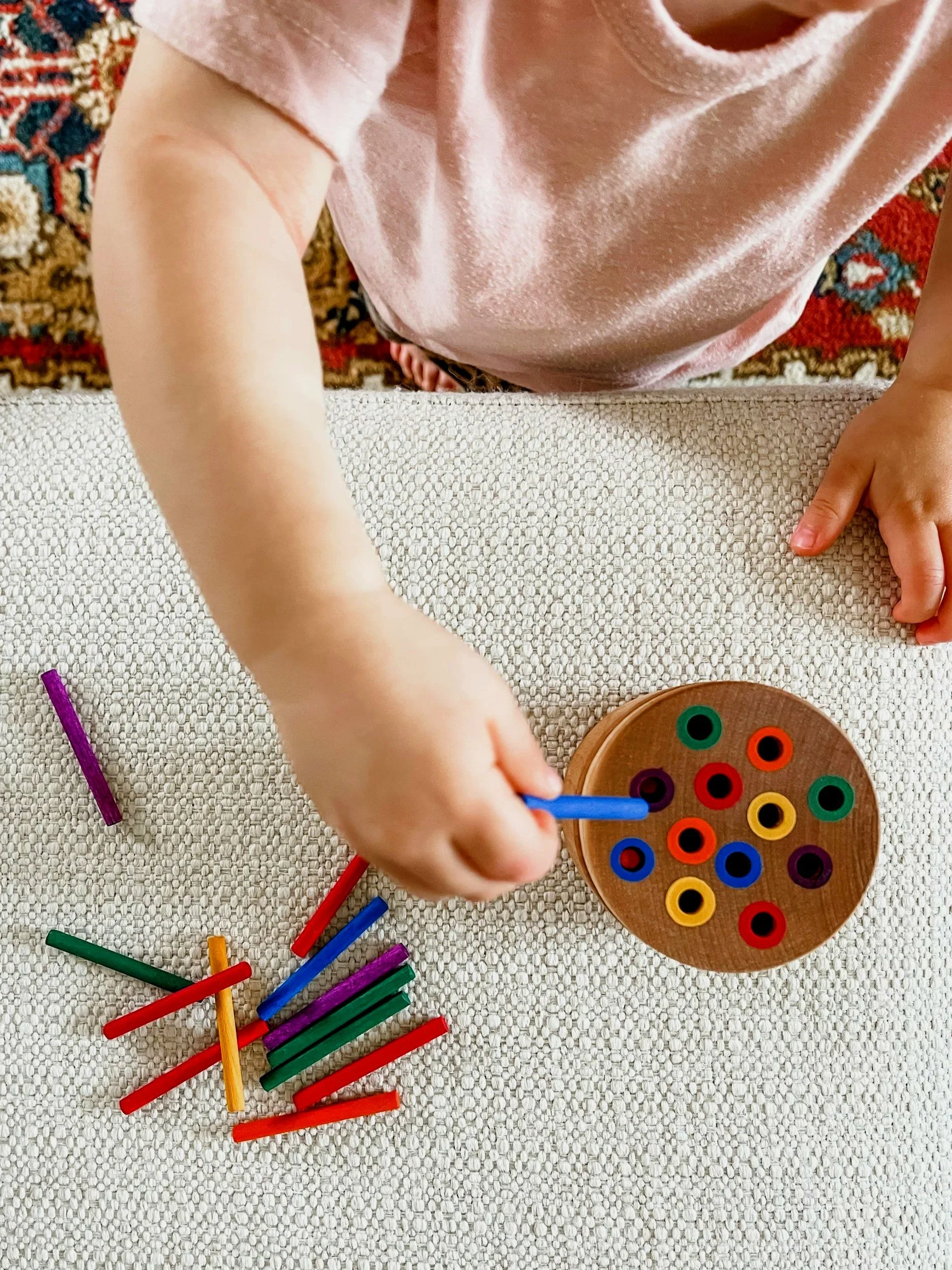 A young child playing a ring tossing game with colorful rings and a wooden stand on a textured white surface.
